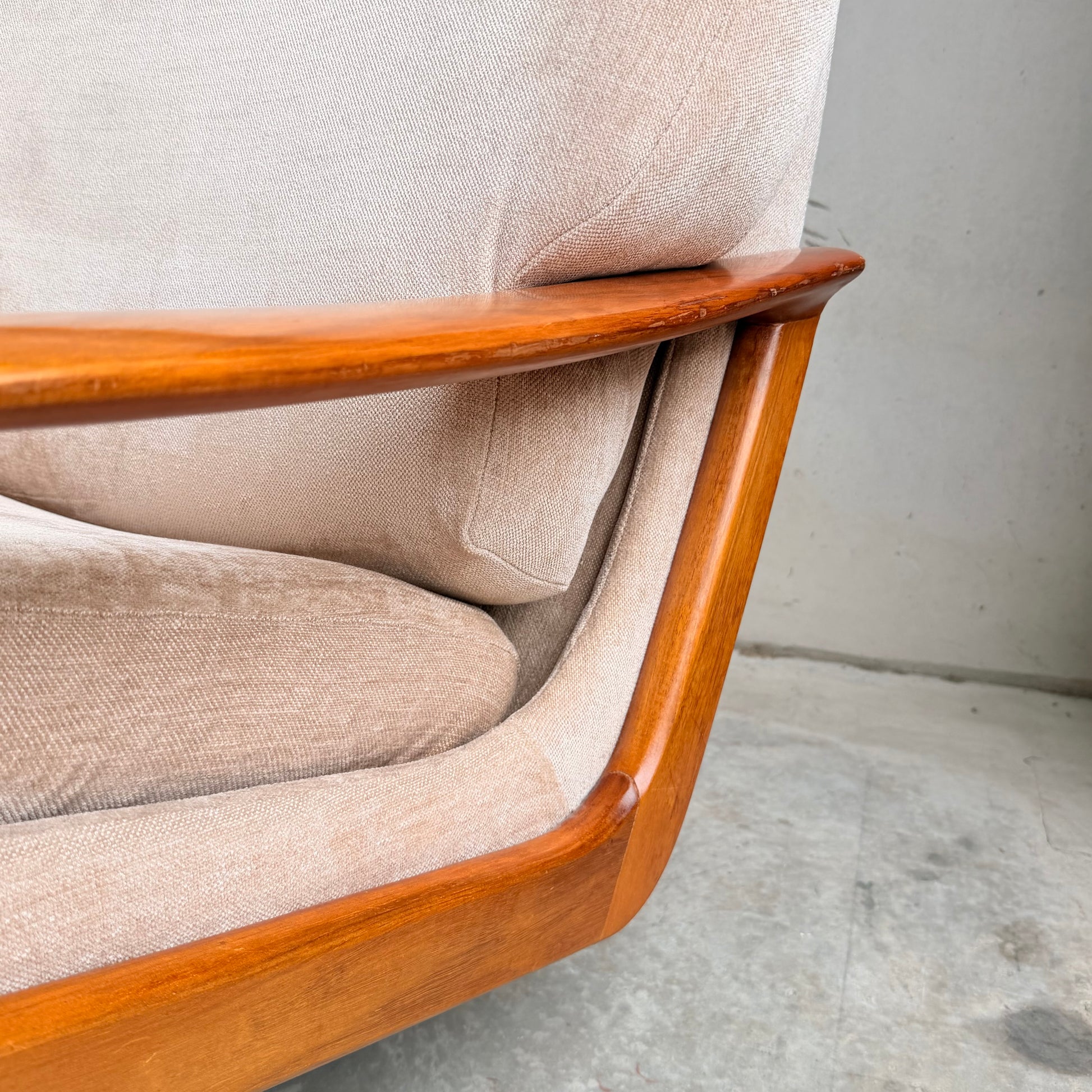 Close-up of a Vintage Mid Century Tessa T21 Swivel Chair (Revive) in cream velvet, featuring a smooth curved wooden frame, set on concrete flooring by a light gray wall—showcasing timeless mid-century design.