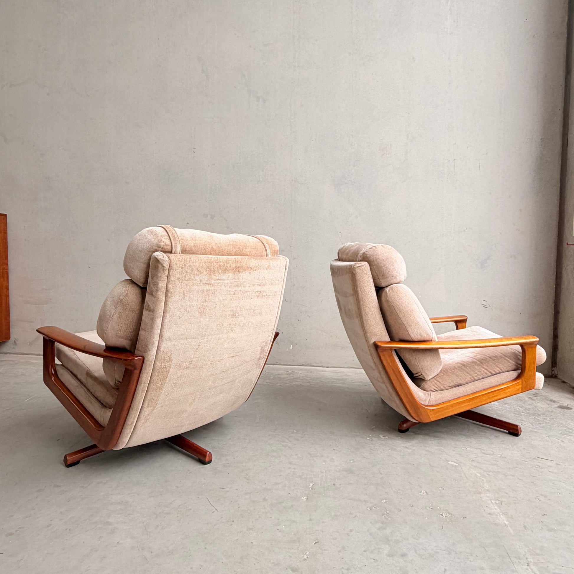Two Vintage Mid Century Tessa T21 Swivel Chairs (Revive) with cream velvet upholstery and wooden frames sit on a concrete floor against a plain, light wall, positioned to highlight their elegant mid-century design and swivel feature.