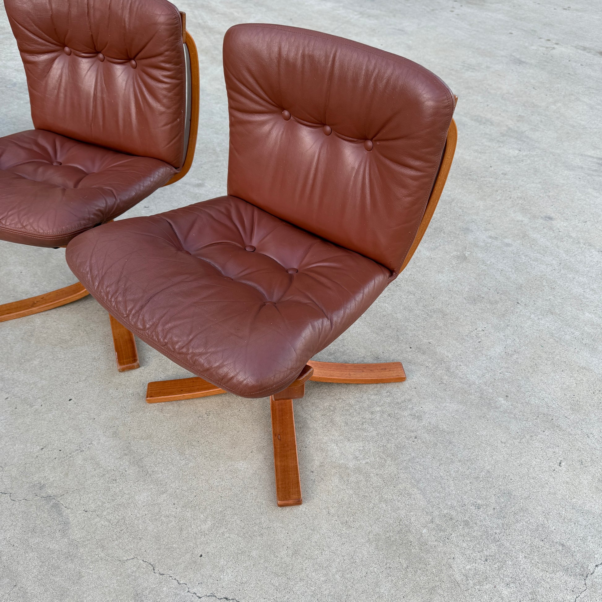 A rare set of 4 vintage Joe Rufenacht lounge chairs in Howe leather with tufted brown cushions and wooden bases sits on a smooth, light concrete surface, highlighting Scandinavian-inspired, mid-century modern style.