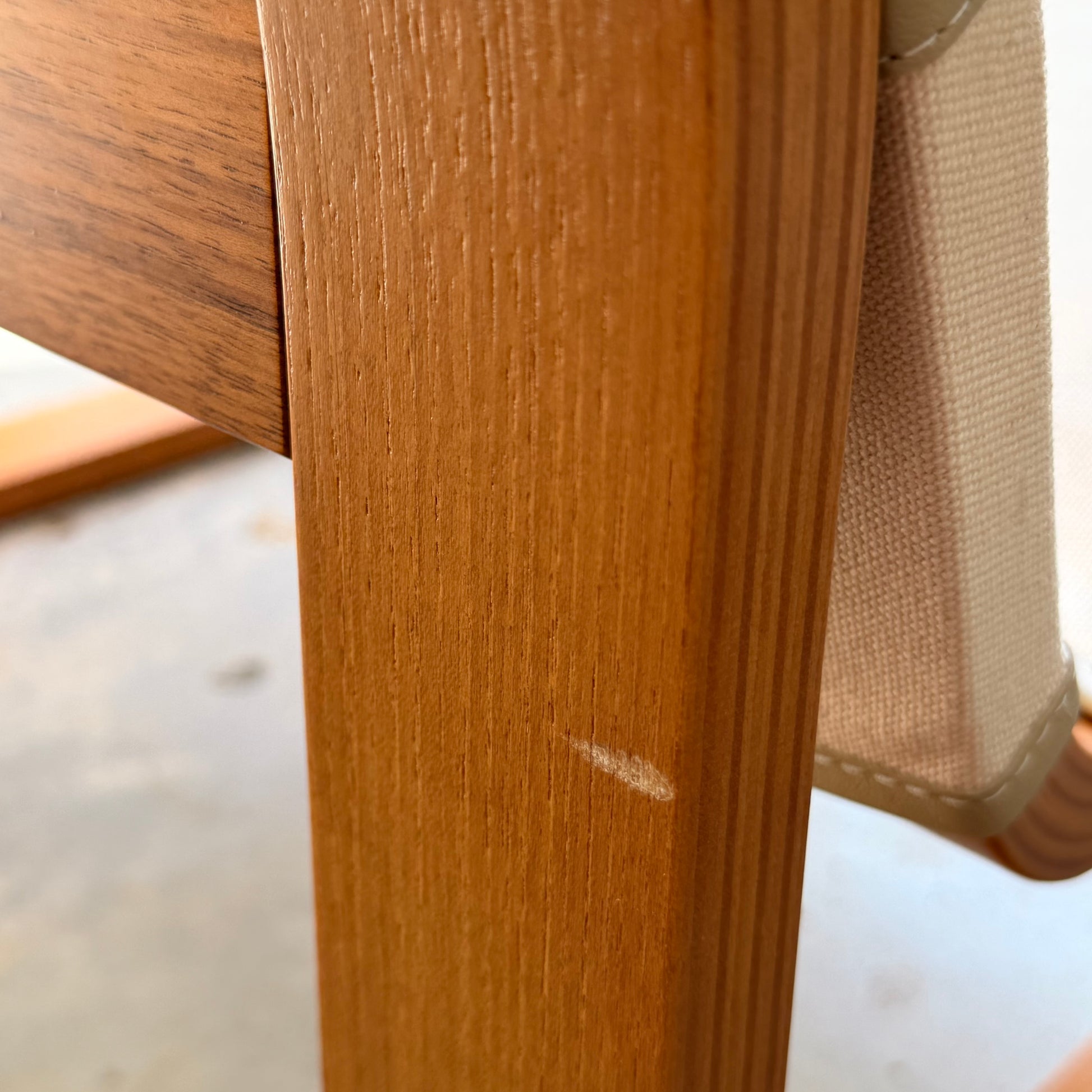 Close-up of a wooden leg from a Pair of Tessa Monaco Arm Chairs - Sage Green Corduroy Like New (Revive), showing a small white scratch. Part of the sage green corduroy fabric is visible in the background.