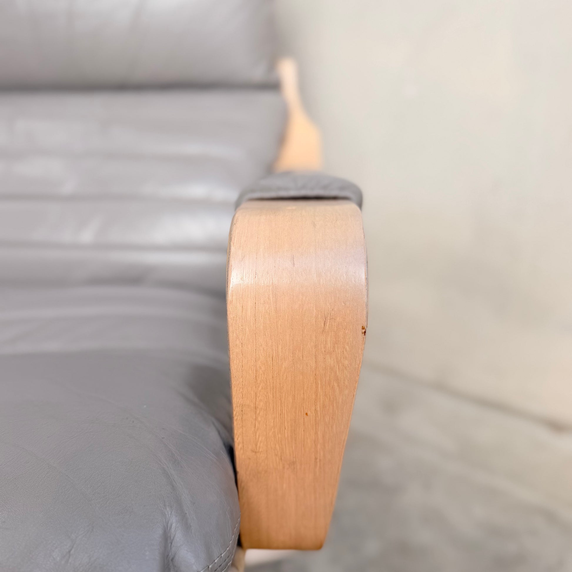 Close-up of a wooden armrest on the Tessa Ferrara Lounge Suite – Complete 5-Piece Set (Revive), showing the textured gray leather and curved design in classic mid-century modern style, with a blurred background and visible floor.
