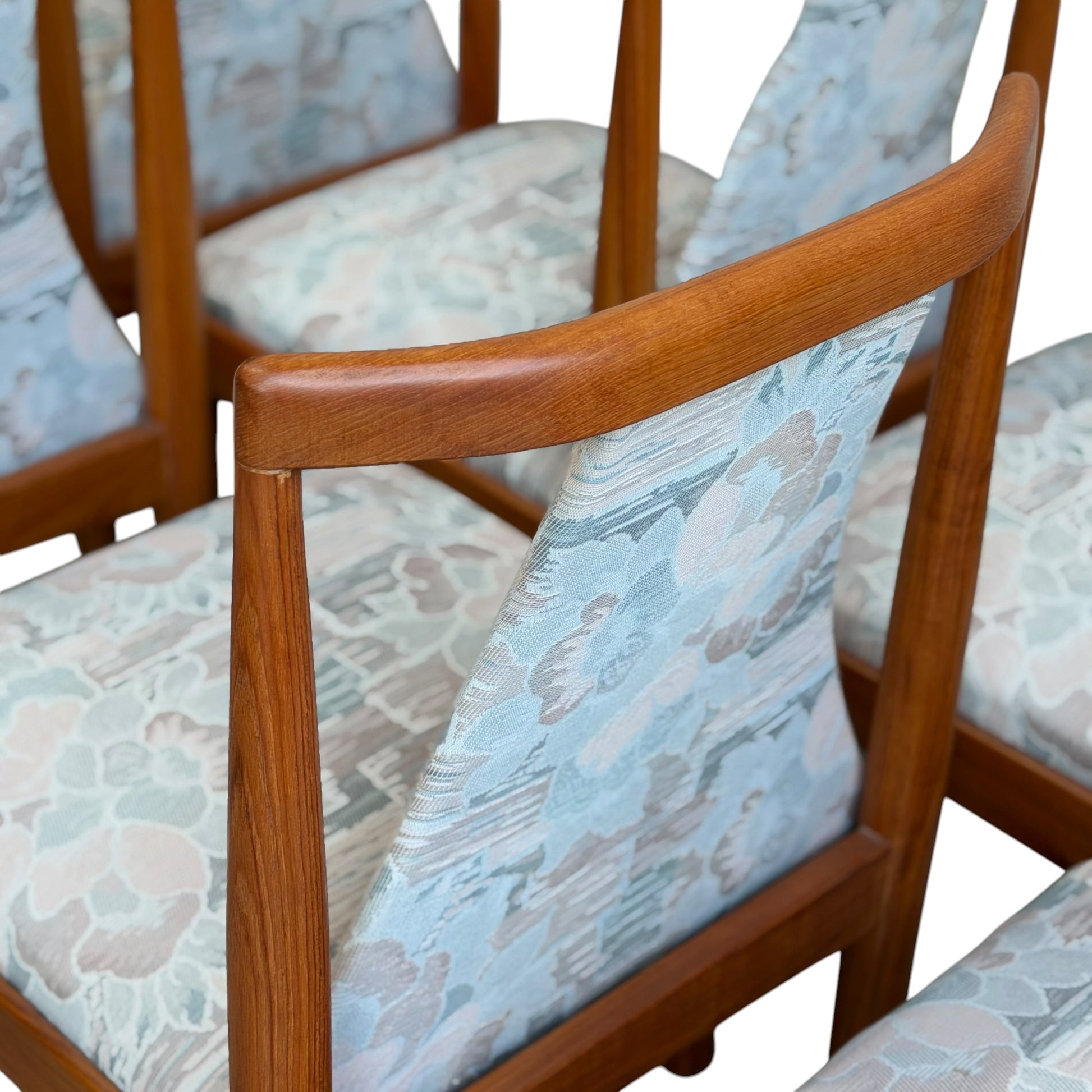 A set of 6 Vintage CRO Teak Dining Chairs (Revive) features mid-century modern warm-toned teak frames and seats and backs upholstered in subtle pastel blue floral fabric, arranged closely together for a stylish dining setup.