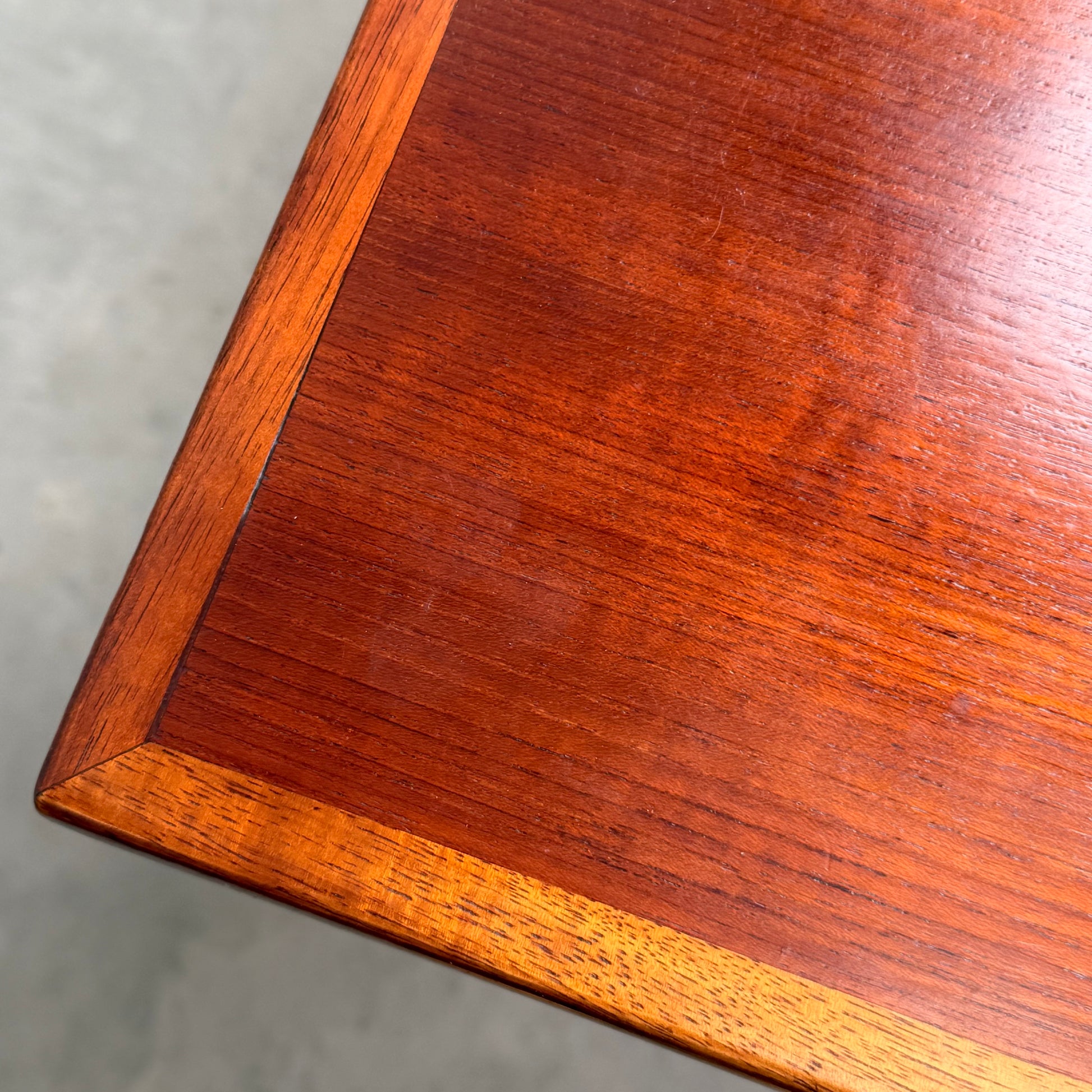 Close-up of the corner of a Vintage Mid-Century Parker 109 Nordic Extension Dining Table (Table Only, Revive), showing its polished finish, visible wood grain, and lighter border against a blurred gray background.