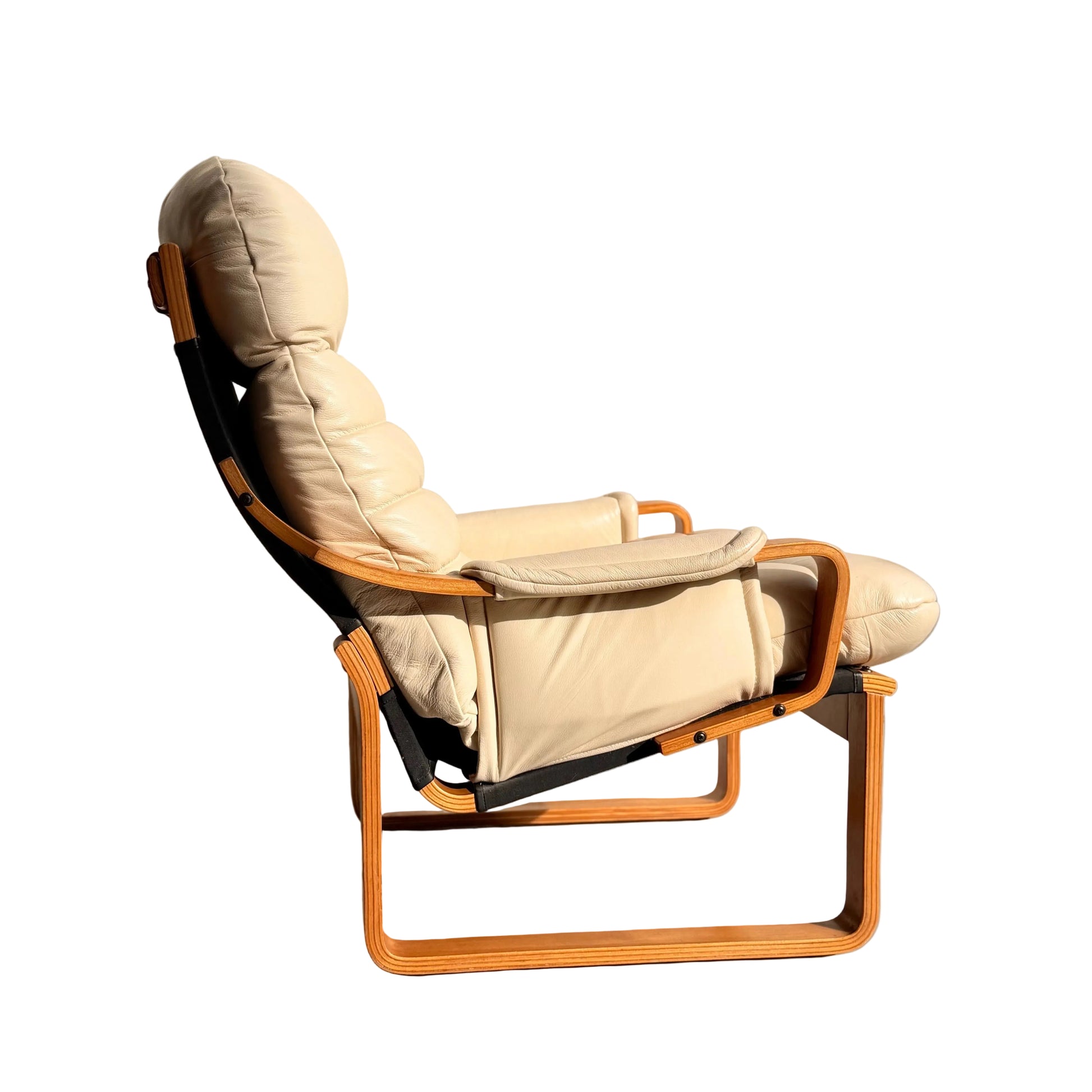 The Tessa Austin Blonde Leather Armchair (Revive) features beige leather upholstery, a padded seat and backrest, and a bentwood frame with armrests, placed against a sunlit wall on a concrete floor.