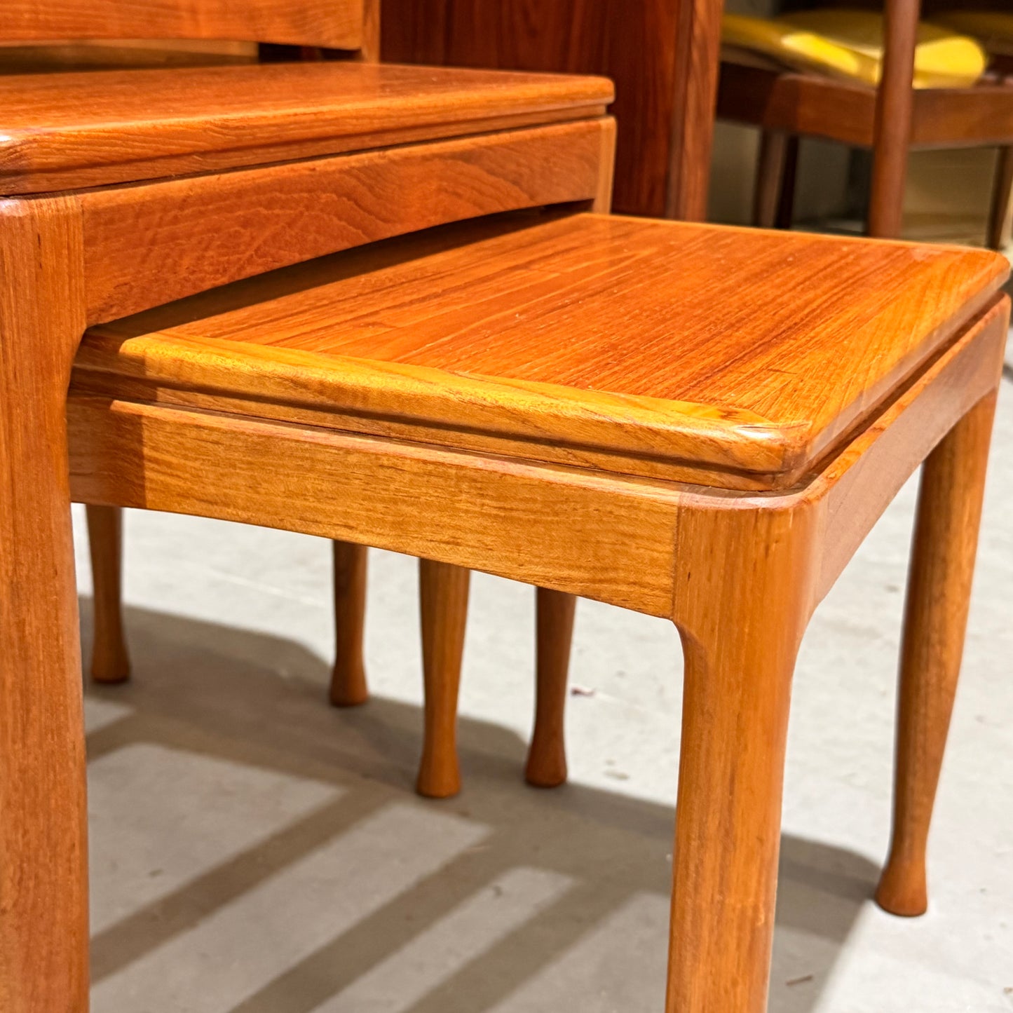 Close-up of the rare Alpa Teak Nesting Tables—set of 3, Australian mid-century modern (Revive), featuring rounded legs and a polished, warm-toned finish, stacked neatly on a light-colored floor.