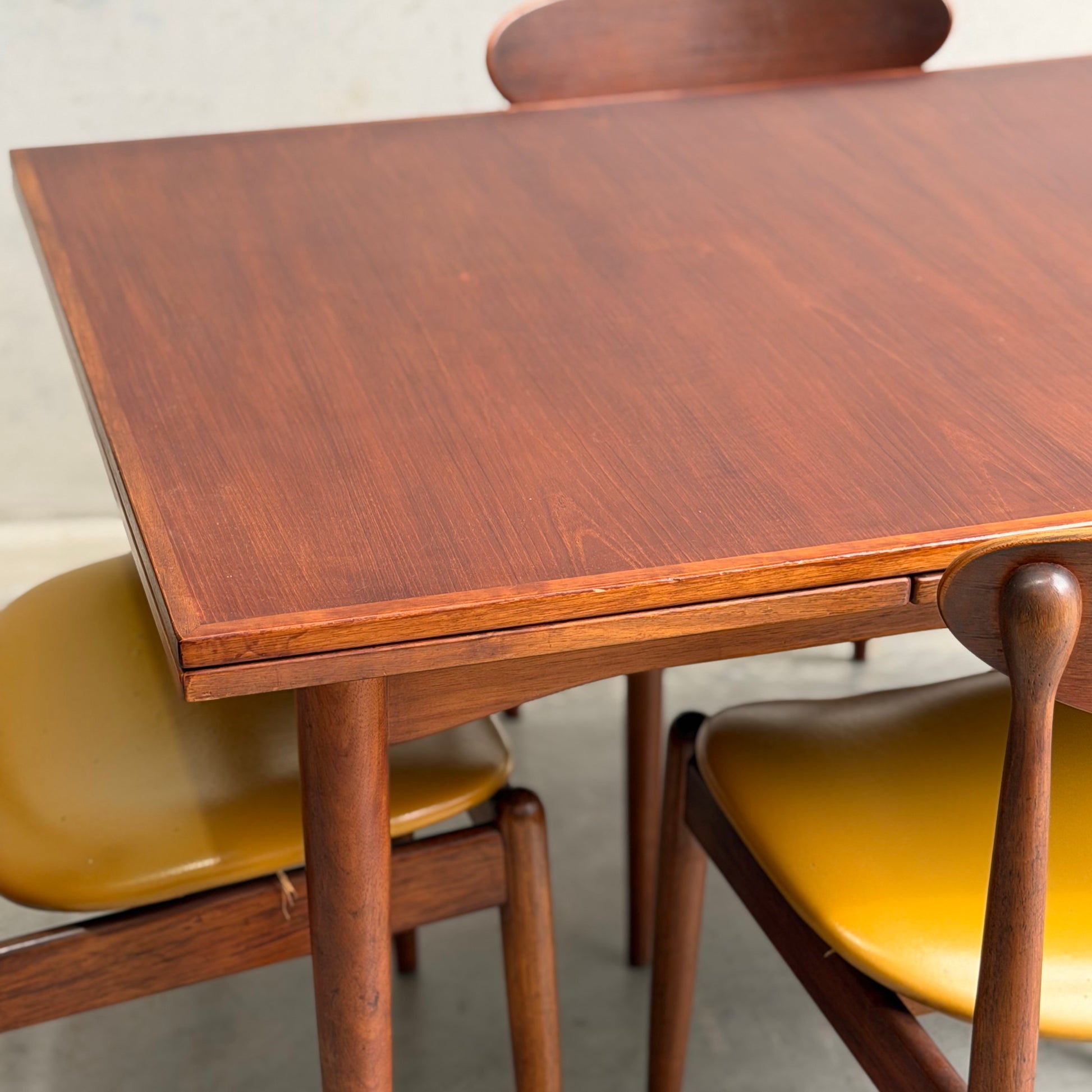 A close-up of the Vintage Mid-Century Parker 109 Nordic Extension Dining Table (Revive), rectangular with rounded edges, is set indoors against a light-colored wall. Matching chairs with curved wooden backs and yellow seats complete the look.