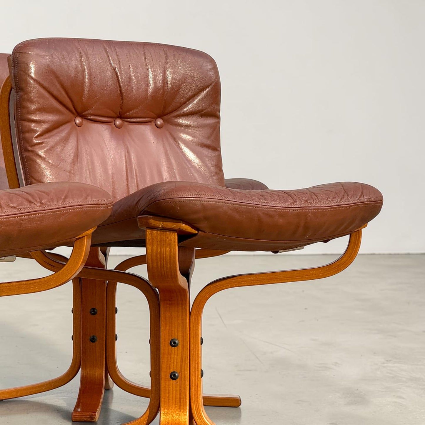 A rare set of 4 vintage Joe Rufenacht lounge chairs with Howe leather upholstery and curved wooden frames are arranged on a light gray floor against a plain white background.