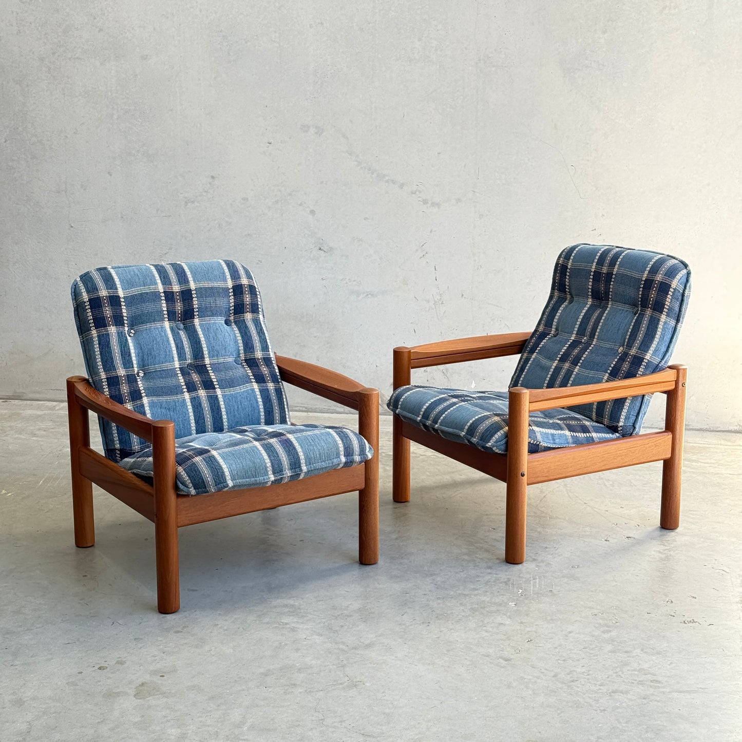 Two restored Domino Møbler armchairs from the Rediscover Blue Plaid Mid-Century Set sit side by side on a light gray concrete floor against a plain, light-colored wall.