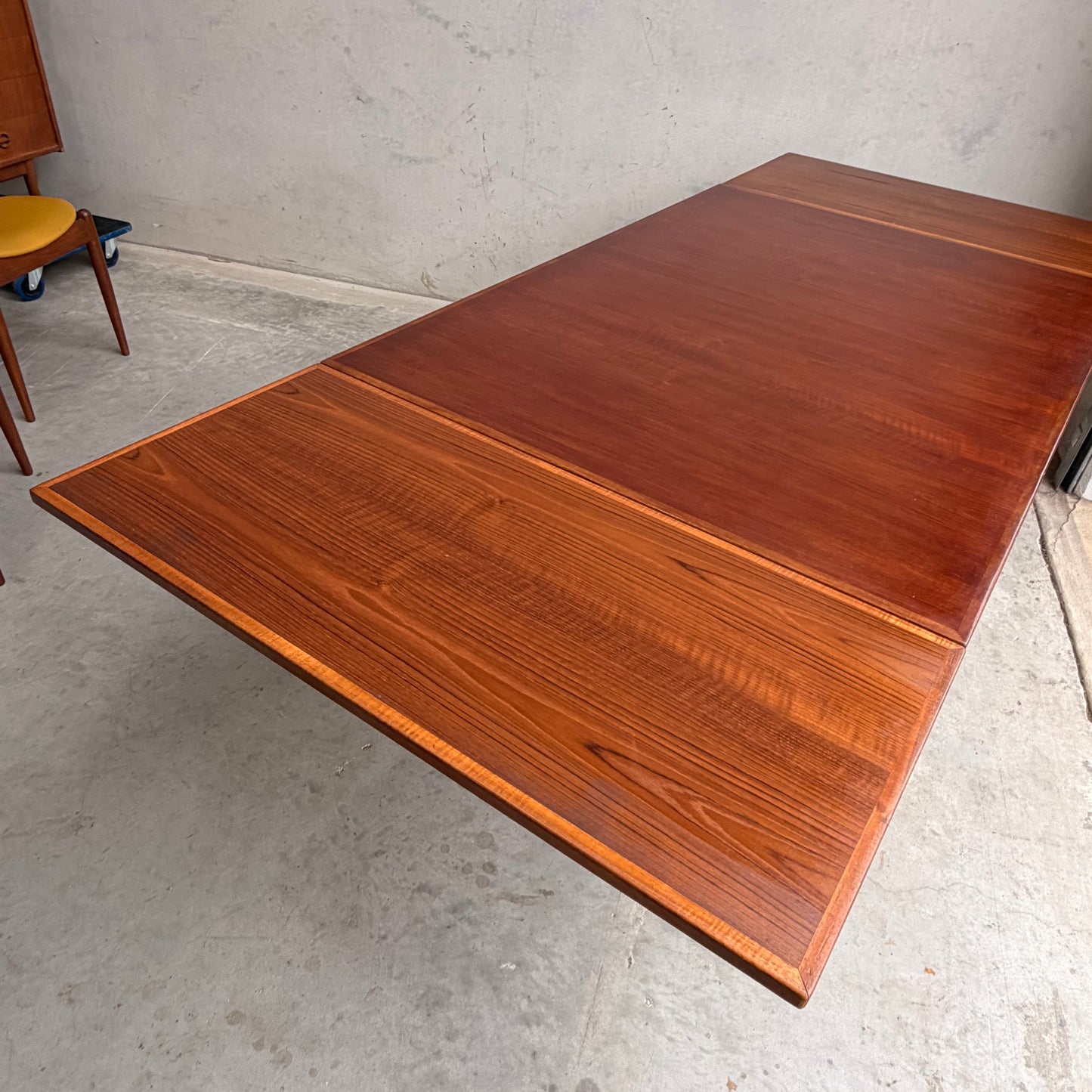 The Vintage Mid-Century Parker 109 Nordic Extension Dining Table - Table Only (Revive) with a rich brown finish stands on a concrete floor, part of a yellow-cushioned chair showing near a plain light wall.