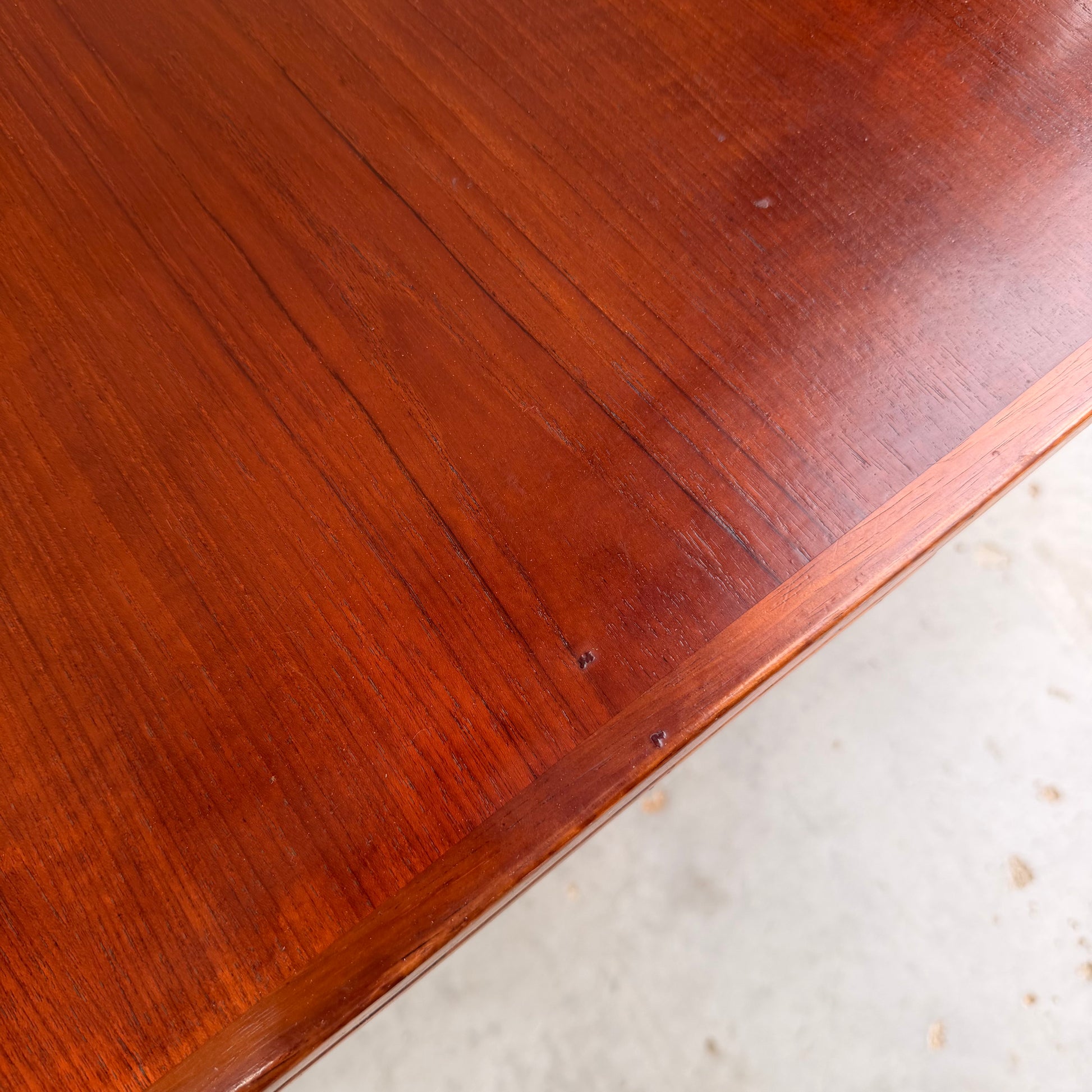 Close-up of the Vintage Mid-Century Parker 109 Nordic Extension Dining Table (Revive) shows its polished teak surface with rich reddish-brown grain, subtle imperfections, and a light floor backdrop that highlights its elegant mid-century modern design.
