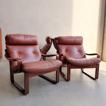 Two brown leather armchairs with wooden frames and tufted cushions evoke mid-century style. Placed side by side, they recall the timeless look of the Tessa T8 Lounge Suite modular two-seater sofa & armchairs (Revive).
