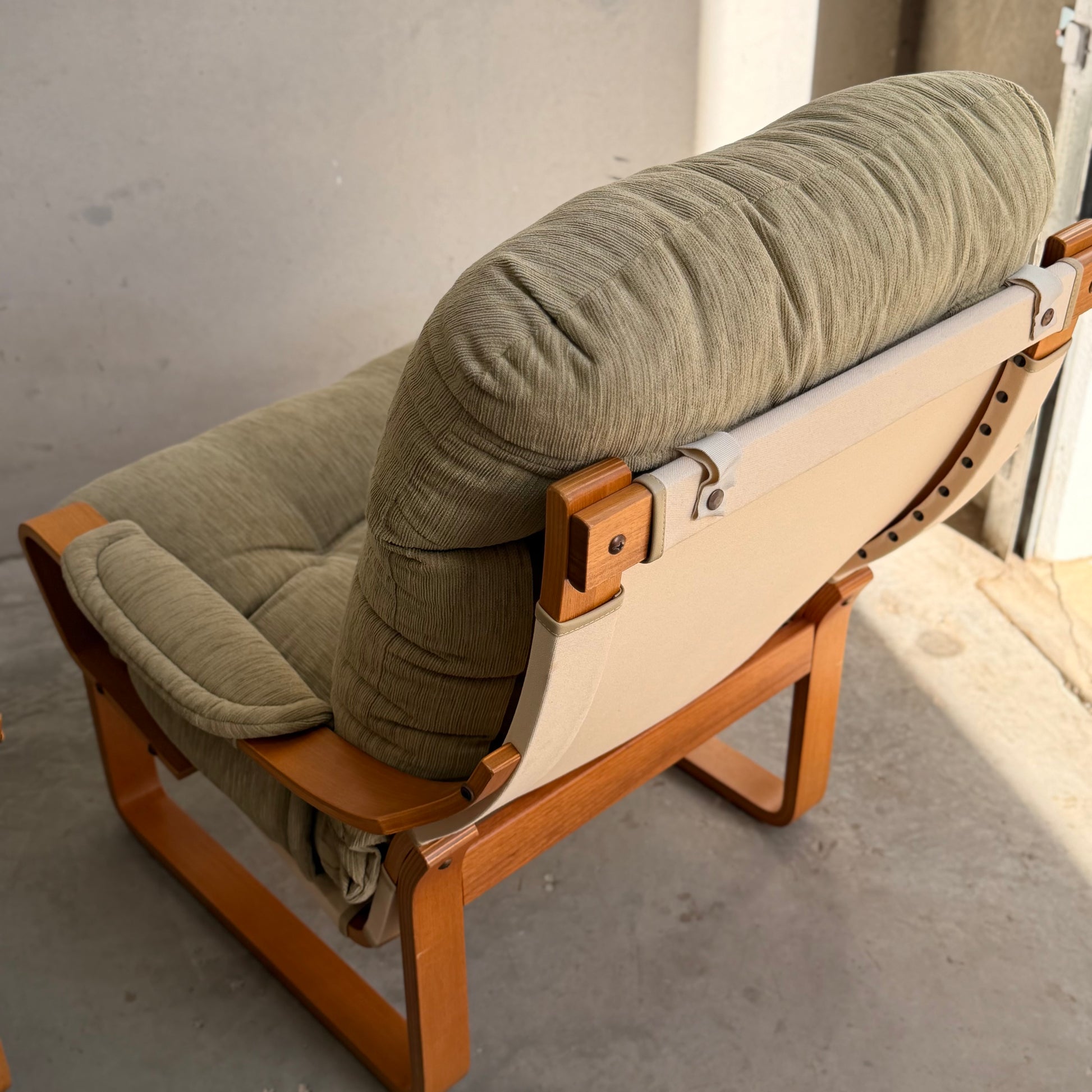 A pair of Tessa Monaco Arm Chairs in sage green corduroy, like new from Revive, features tufted cushions and wooden frames, positioned on a concrete floor in a sunlit room with neutral walls.