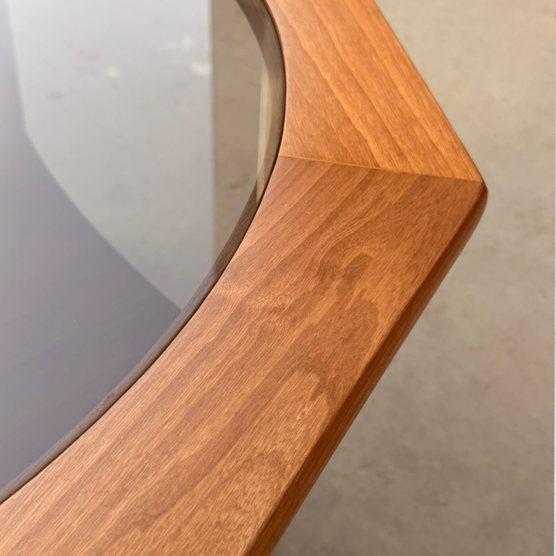 Close-up of the Octagonal Mid Century Coffee Table by Kalmar Furniture, featuring smooth hardwood joints and a smoked glass magazine rack. The warm natural finish shines against a softly blurred neutral background.