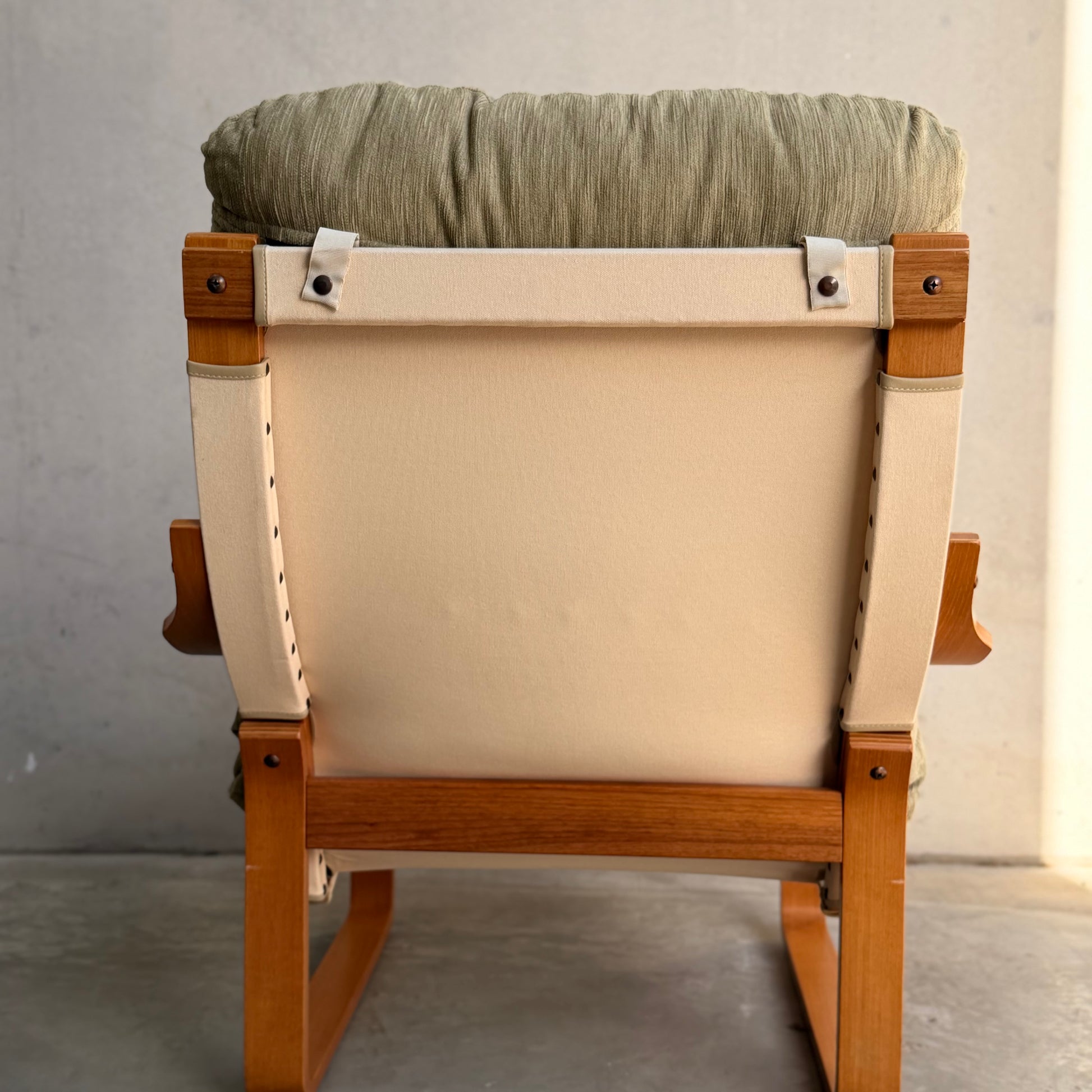 A pair of Tessa Monaco Arm Chairs in sage green corduroy, like new (Revive), with beige fabric backing and wooden frames, shown from behind against a light gray wall.
