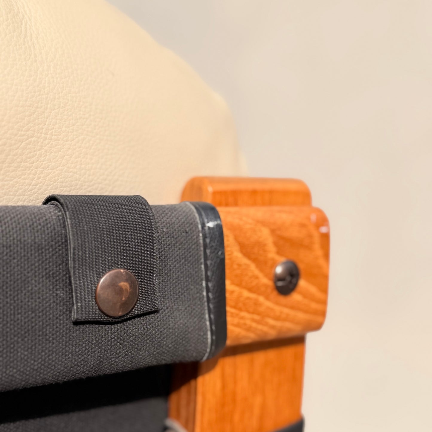 Close-up of the Tessa Austin Blonde Leather Armchair (Revive) corner, showing light tan leather upholstery, a warm wood frame, and a black fabric strap with a metallic button. Background is softly blurred.