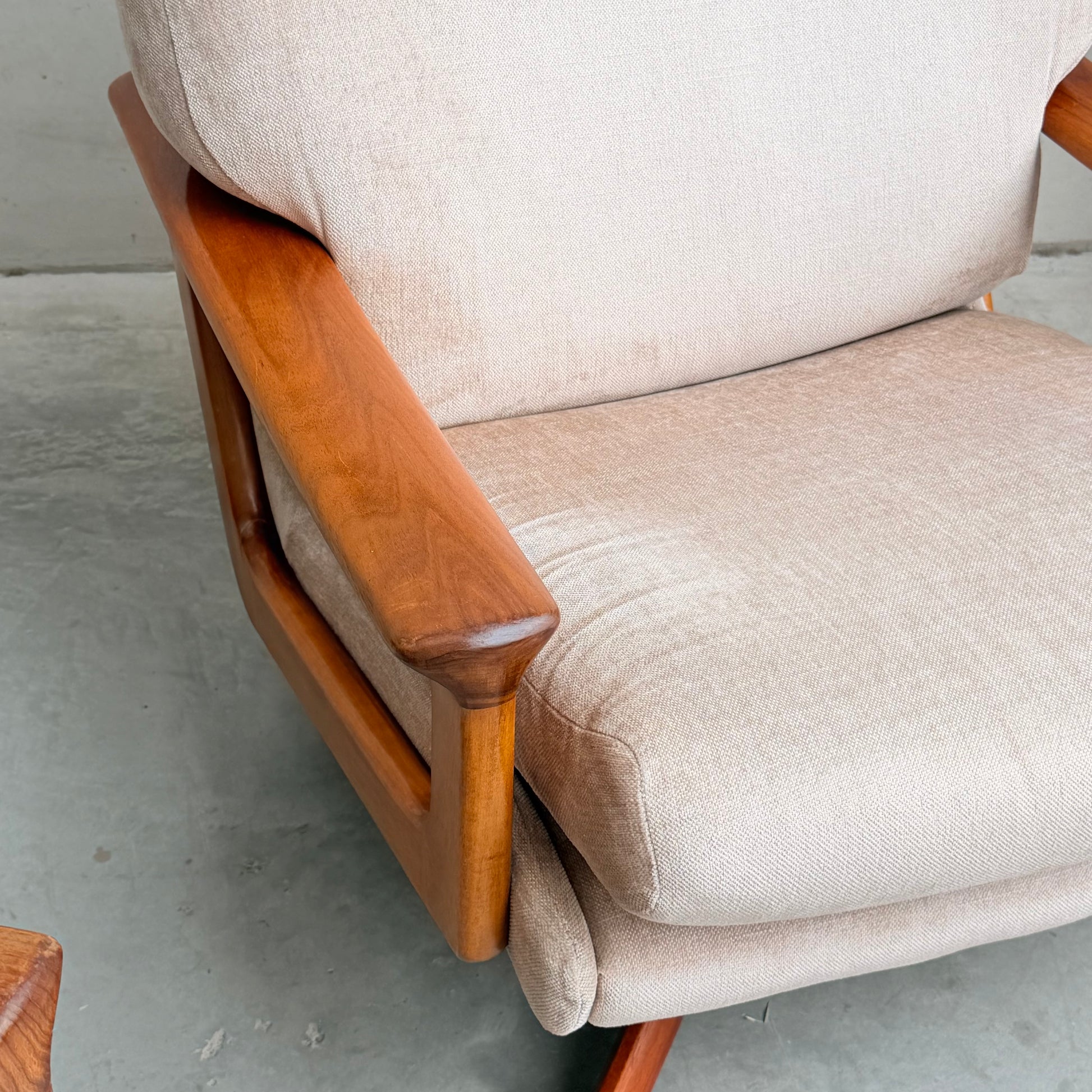 Close-up of the Vintage Mid Century Tessa T21 Swivel Chair (Revive) featuring light beige textured fabric and warm polished wood armrests and frame, echoing mid-century style. Shown atop a gray concrete floor.