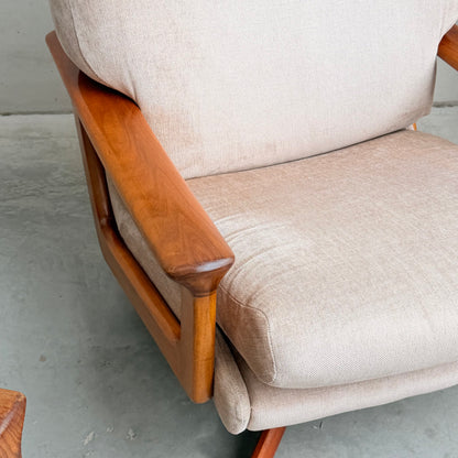 Close-up of the Vintage Mid Century Tessa T21 Swivel Chair (Revive) featuring light beige textured fabric and warm polished wood armrests and frame, echoing mid-century style. Shown atop a gray concrete floor.