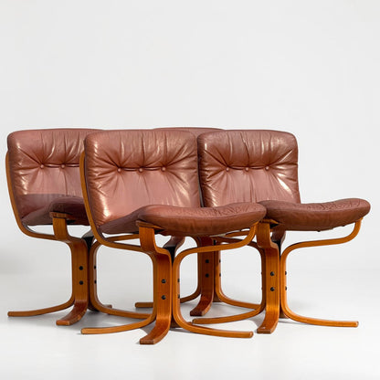 A rare set of 4 vintage Joe Rufenacht lounge chairs with curved wooden frames and Howe leather upholstery are arranged in a staggered row on a plain white background.