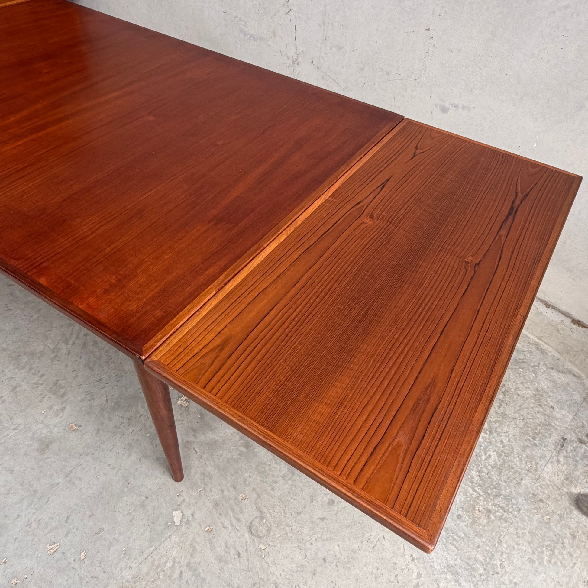 A close-up of the Vintage Mid-Century Parker 109 Nordic Extension Dining Table – Table Only (Revive), showcasing its warm reddish-brown wood grain and extended leaf, set against a plain concrete background.