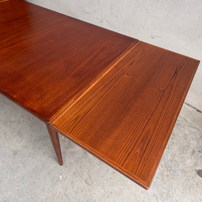 A close-up of the Vintage Mid-Century Parker 109 Nordic Extension Dining Table – Table Only (Revive), showcasing its warm reddish-brown wood grain and extended leaf, set against a plain concrete background.