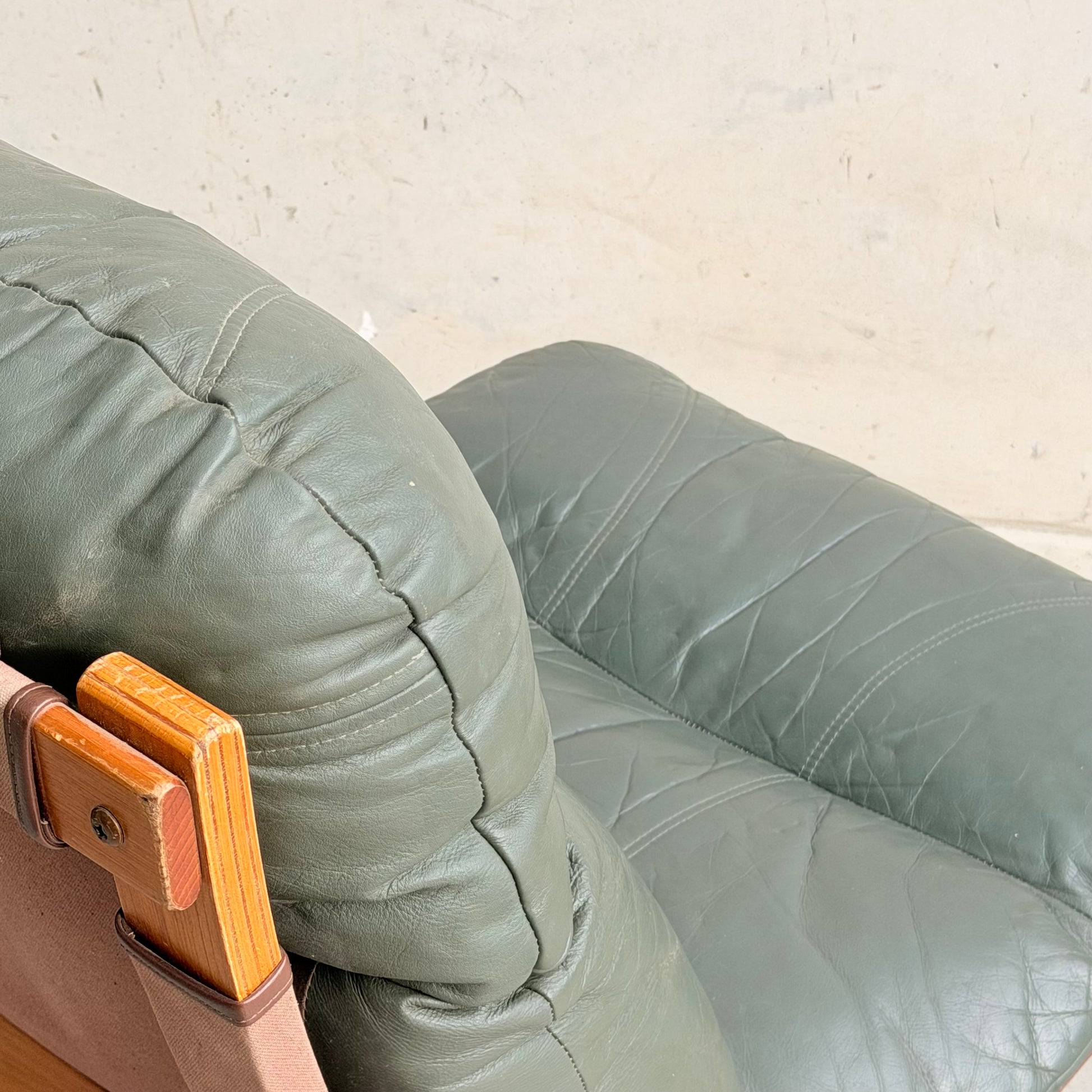 Close-up view of the Tessa Vintage Single No Arm Monaco Armchair – Forest Green (Revive), a mid-century style armchair with green leather upholstery and wooden frame details, set against a plain light-colored wall.