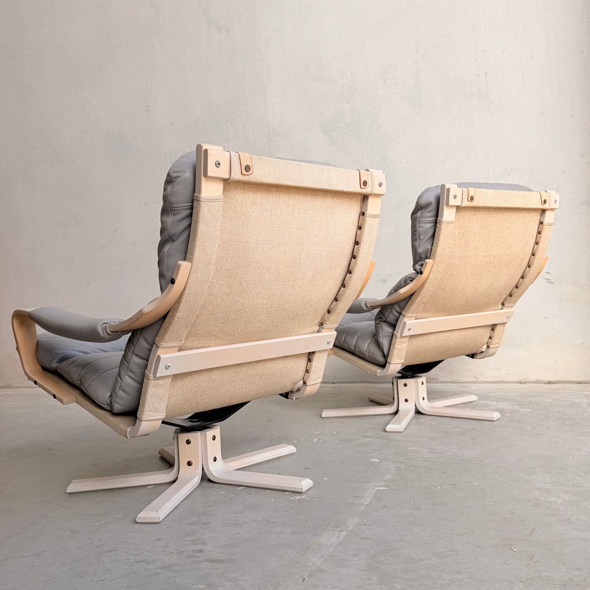 A Pair of Tessa Ferrara Swivel Armchairs (Revive) with light wood frames, beige fabric backs, and gray cushioned seats sits side by side, showcasing iconic mid-century Australian style reminiscent of classic Tessa Furniture.