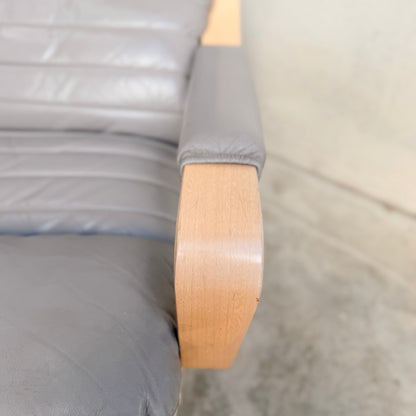 Close-up of a pair of gray leather Tessa Ferrara Swivel Armchairs (Revive) with padded armrests and light wood frames on a polished concrete floor, highlighting their iconic mid-century Australian design.