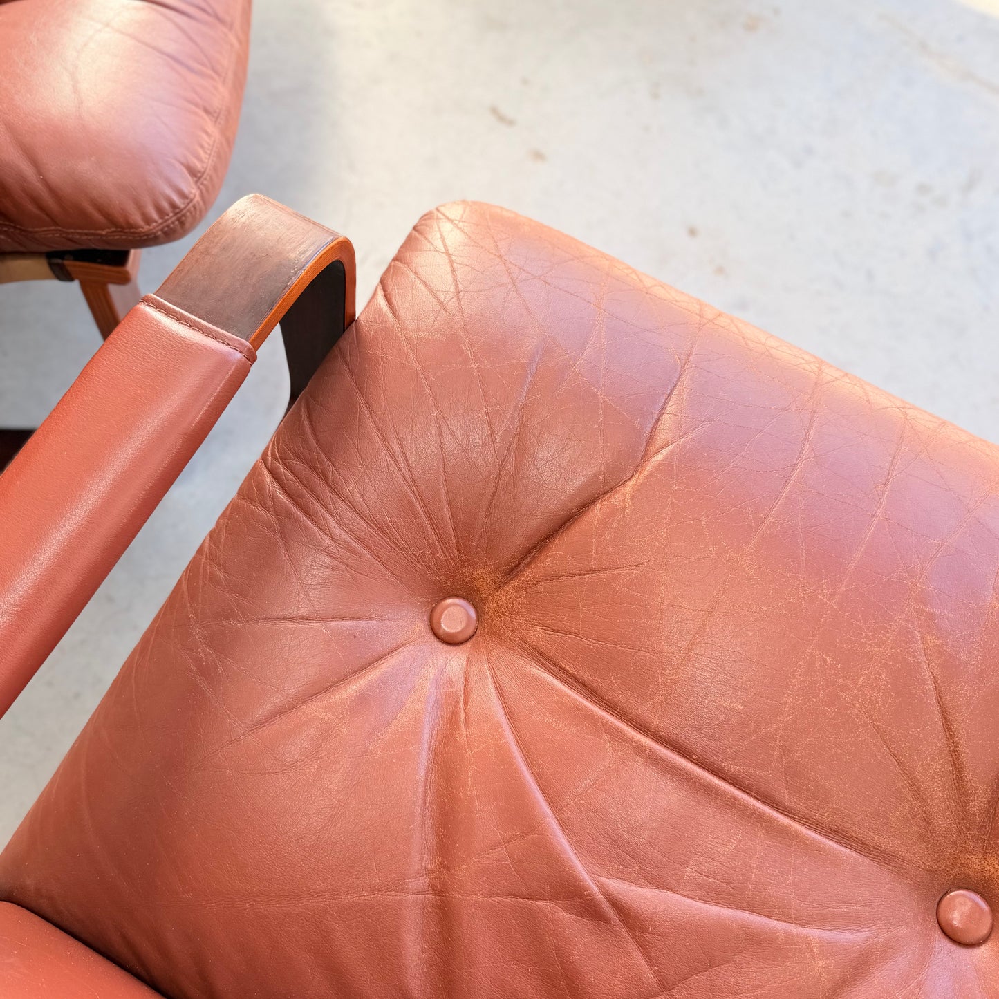 Close-up of the Tessa T8 Lounge Suite modular two-seater sofa & armchairs (Revive): vintage brown leather with creases, central button tuft, and wooden armrest, capturing iconic mid-century modern style on a light floor.
