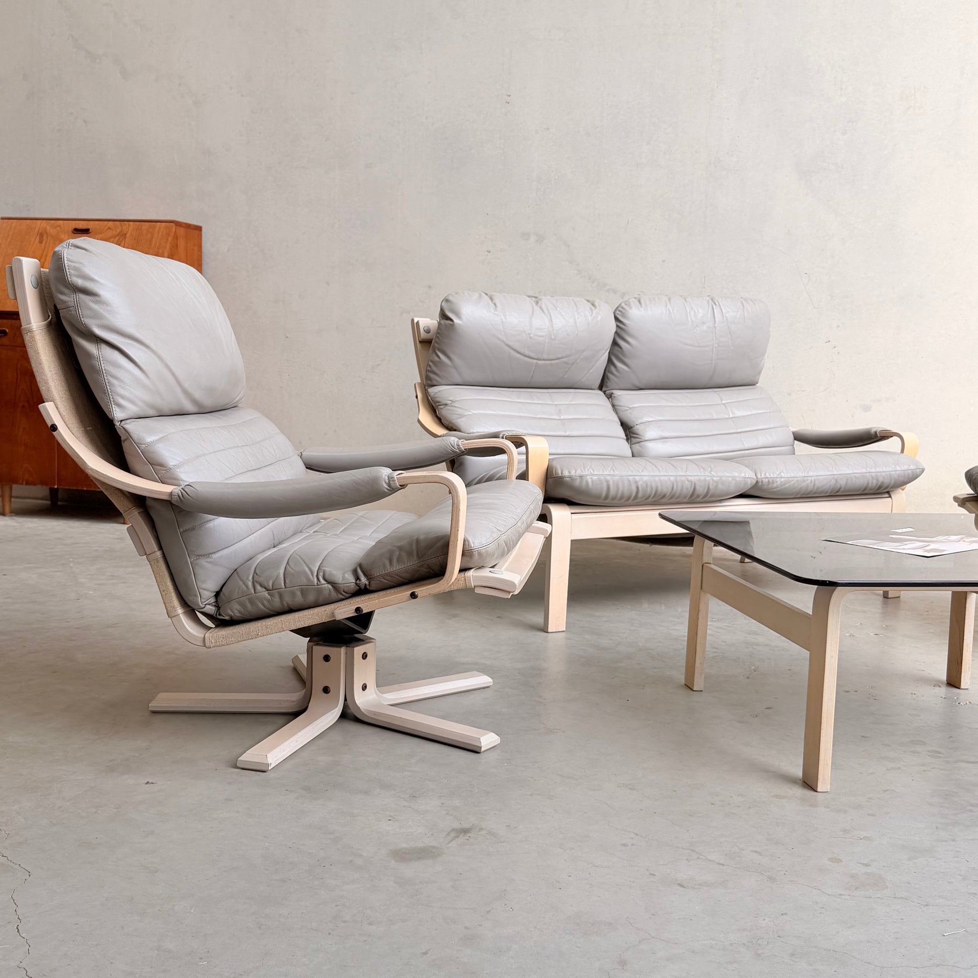 The Tessa Ferrara Lounge Suite – Complete 5-Piece Set (Revive) features a gray cushioned armchair, matching two-seat sofa, and glass-topped coffee table with light wood frames, perfect for modern living rooms.