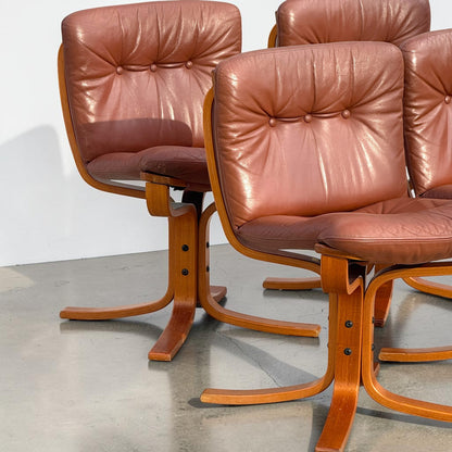 A rare set of 4 vintage Joe Rufenacht lounge chairs in Howe leather with curved wooden frames are arranged on a polished concrete floor against a plain white background.