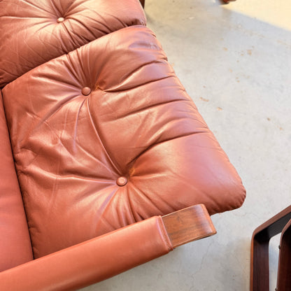 Close-up of a tufted, brown leather cushion on the Tessa T8 Lounge Suite modular two-seater sofa & armchairs (Revive), mid-century modern style with wooden armrests, set on a light-colored concrete floor.