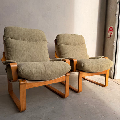 A Pair of Tessa Monaco Arm Chairs in sage green corduroy, like new (Revive), sit side by side on a concrete floor against a light wall, sunlight streaming in to highlight their cushioned mid-century charm.