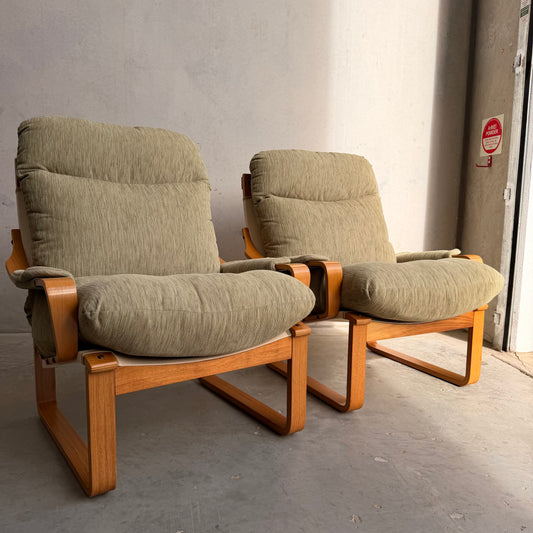 A Pair of Tessa Monaco Arm Chairs in sage green corduroy, like new (Revive), sit side by side on a concrete floor against a light wall, sunlight streaming in to highlight their cushioned mid-century charm.