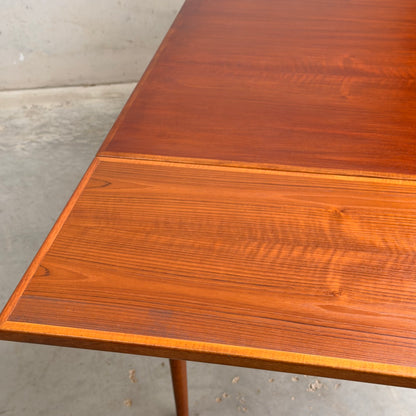 A close-up of the Vintage Mid-Century Parker 109 Nordic Extension Dining Table (Revive), highlighting its wood grain and texture. The table stands on a concrete floor by a light-colored wall.