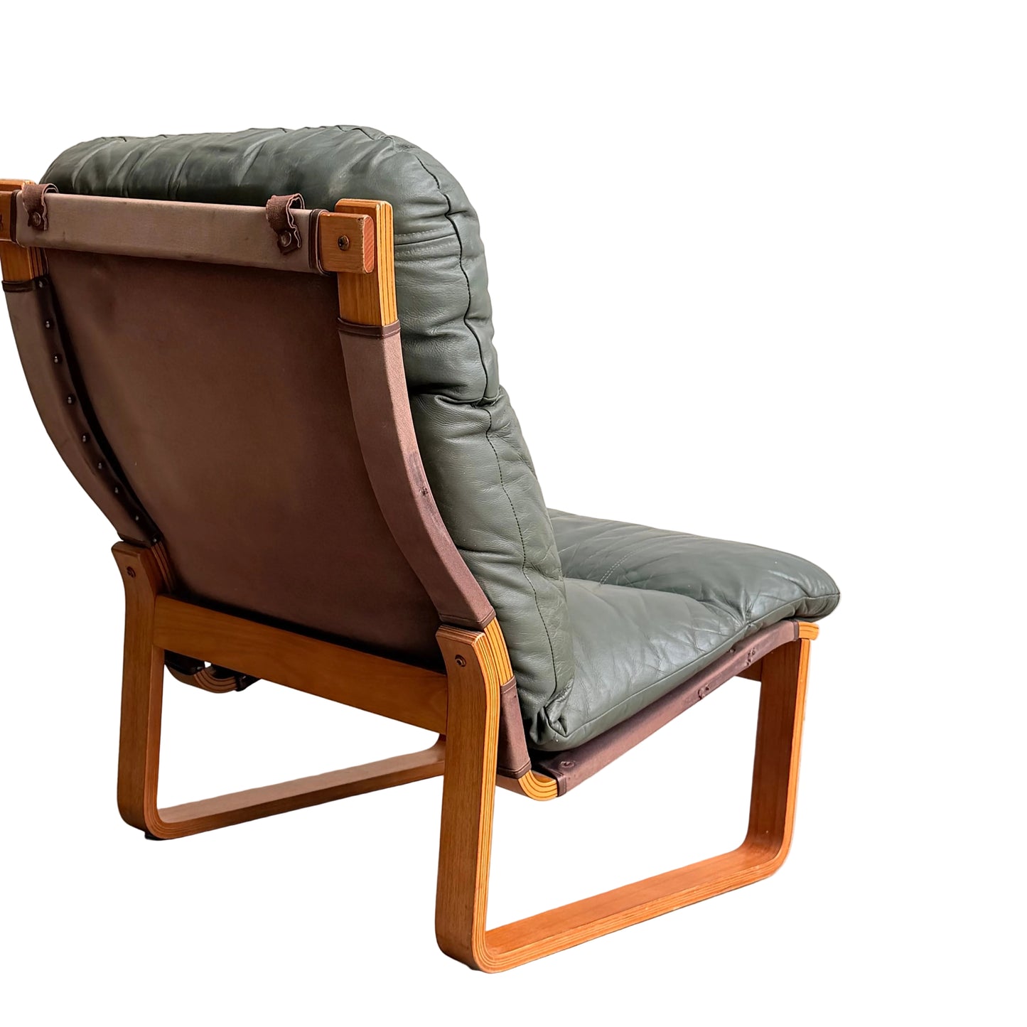 The Tessa Vintage Single No Arm Monaco Armchair in Forest Green (Revive) features a wooden frame and green leather cushion, placed against a plain light wall and concrete floor with brown leather accents.