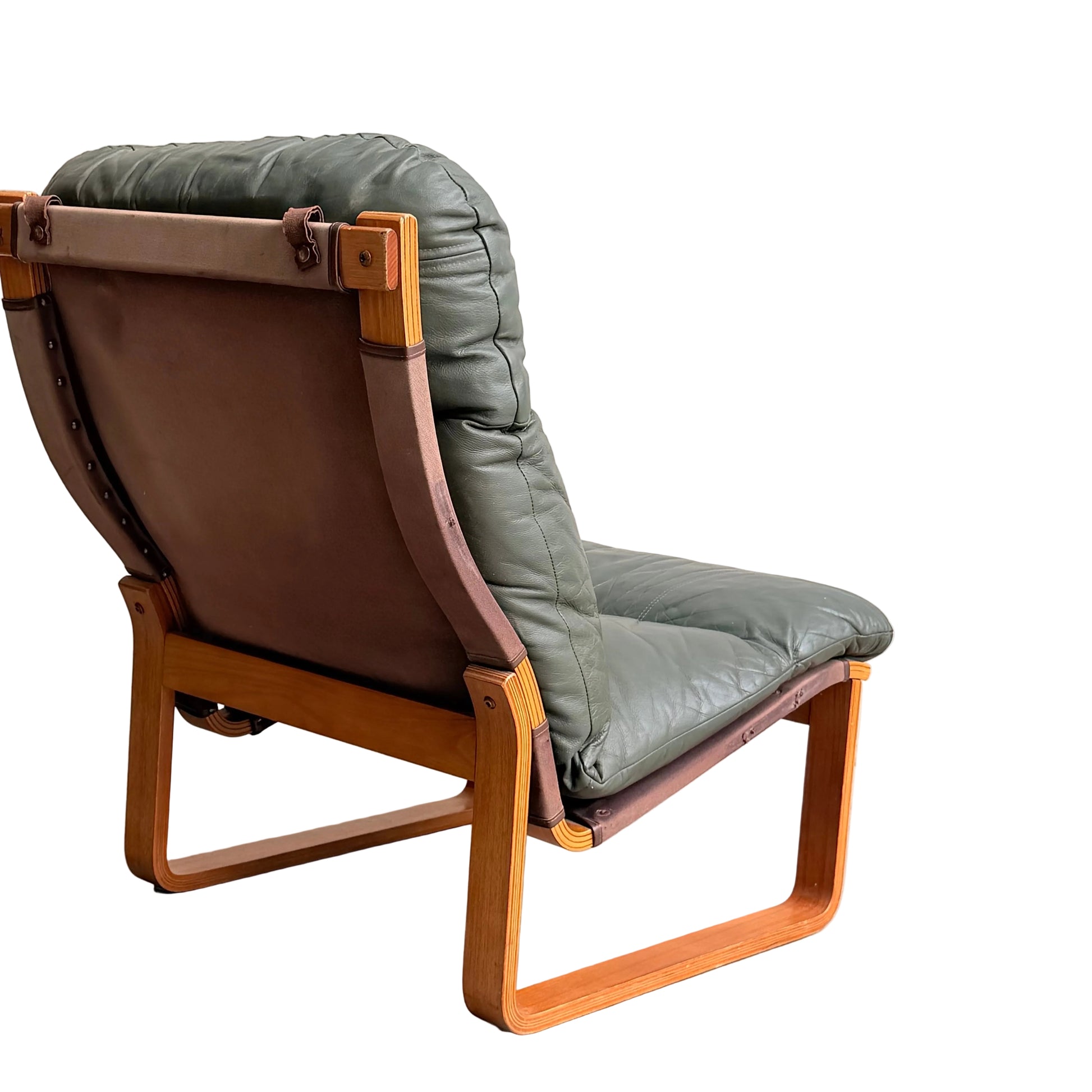 The Tessa Vintage Single No Arm Monaco Armchair in Forest Green (Revive) features a wooden frame and green leather cushion, placed against a plain light wall and concrete floor with brown leather accents.