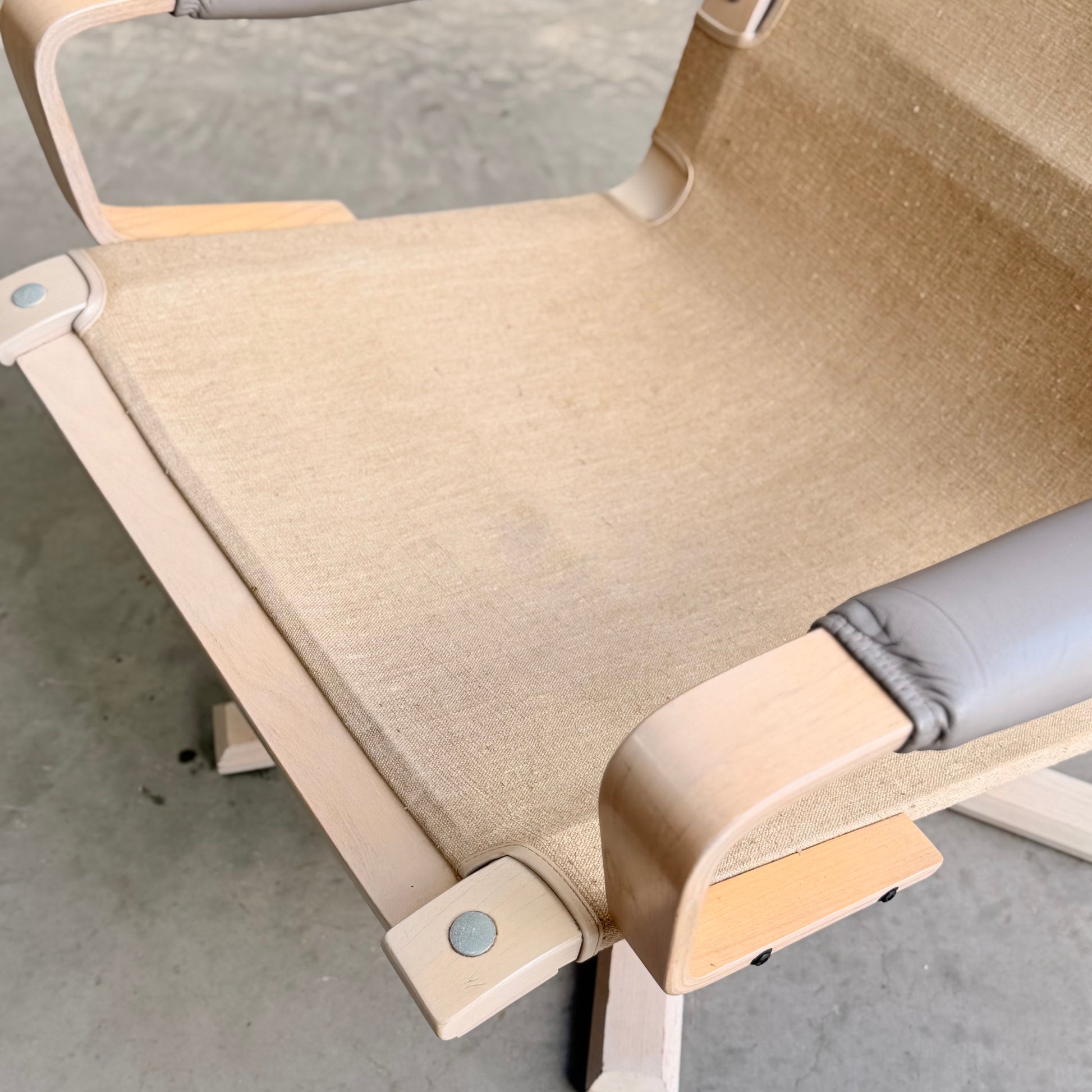 A close-up of a Pair of Tessa Ferrara Swivel Armchairs (Revive) with light wooden frames, beige canvas seats, and gray padded armrests, inspired by vintage Tessa Furniture and mid-century Australian design on a concrete floor.