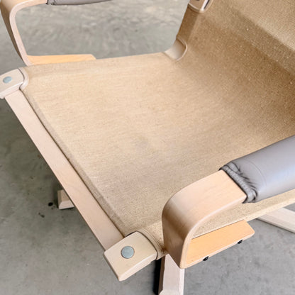 A close-up of a Pair of Tessa Ferrara Swivel Armchairs (Revive) with light wooden frames, beige canvas seats, and gray padded armrests, inspired by vintage Tessa Furniture and mid-century Australian design on a concrete floor.
