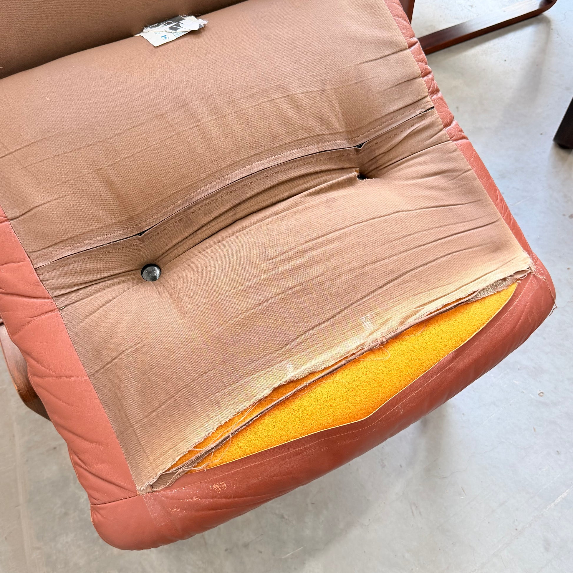 A close-up of a Tessa T8 Lounge Suite modular two-seater sofa armchair seat with torn upholstery, exposing yellow foam padding. The fabric is stretched, discolored, and a central button remains visible.