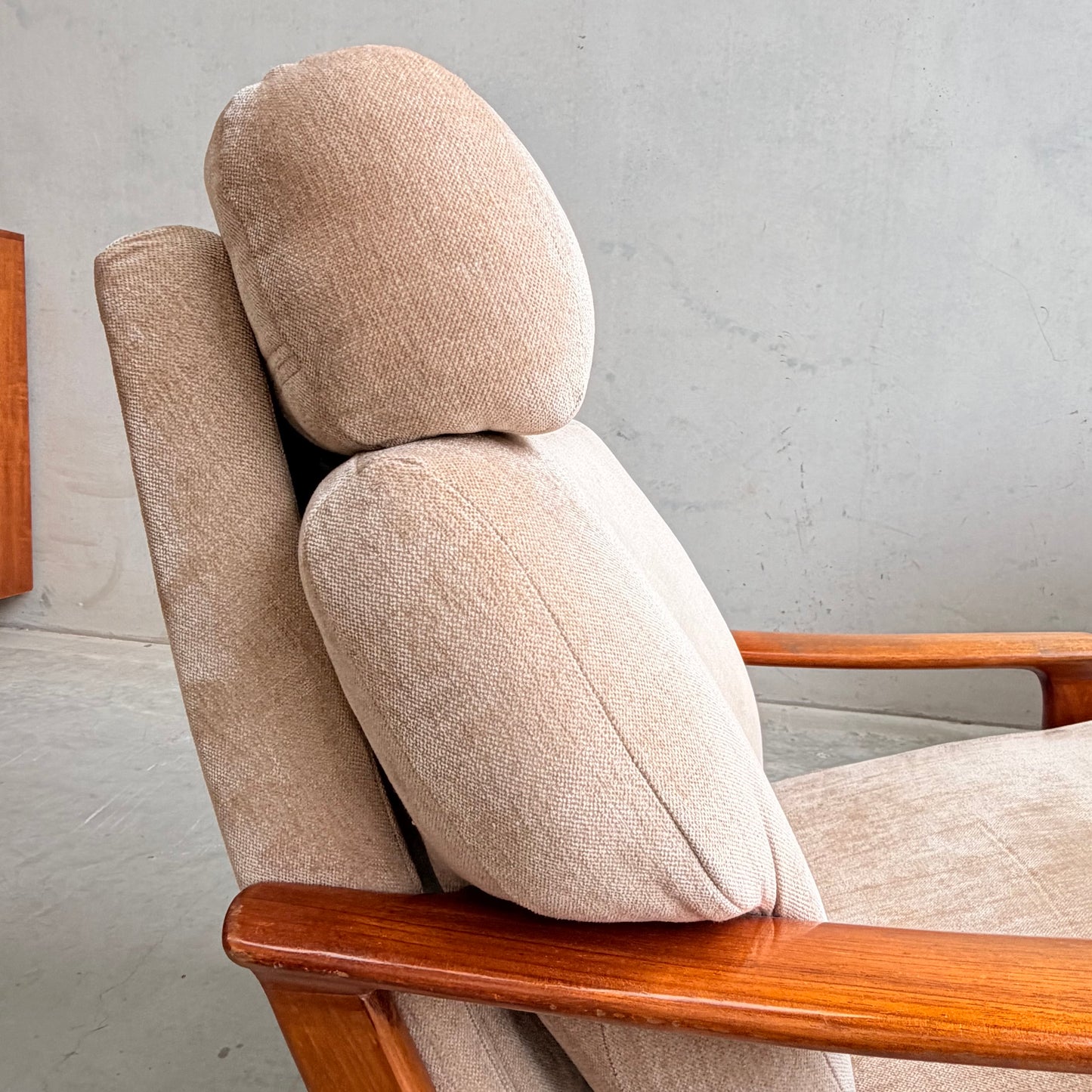 A close-up side view of the Vintage Mid Century Tessa T21 Swivel Chair (Revive) in cream velvet with wooden armrests, thick cushioned headrest and backrest, highlights its timeless mid-century style against a plain light-colored wall.
