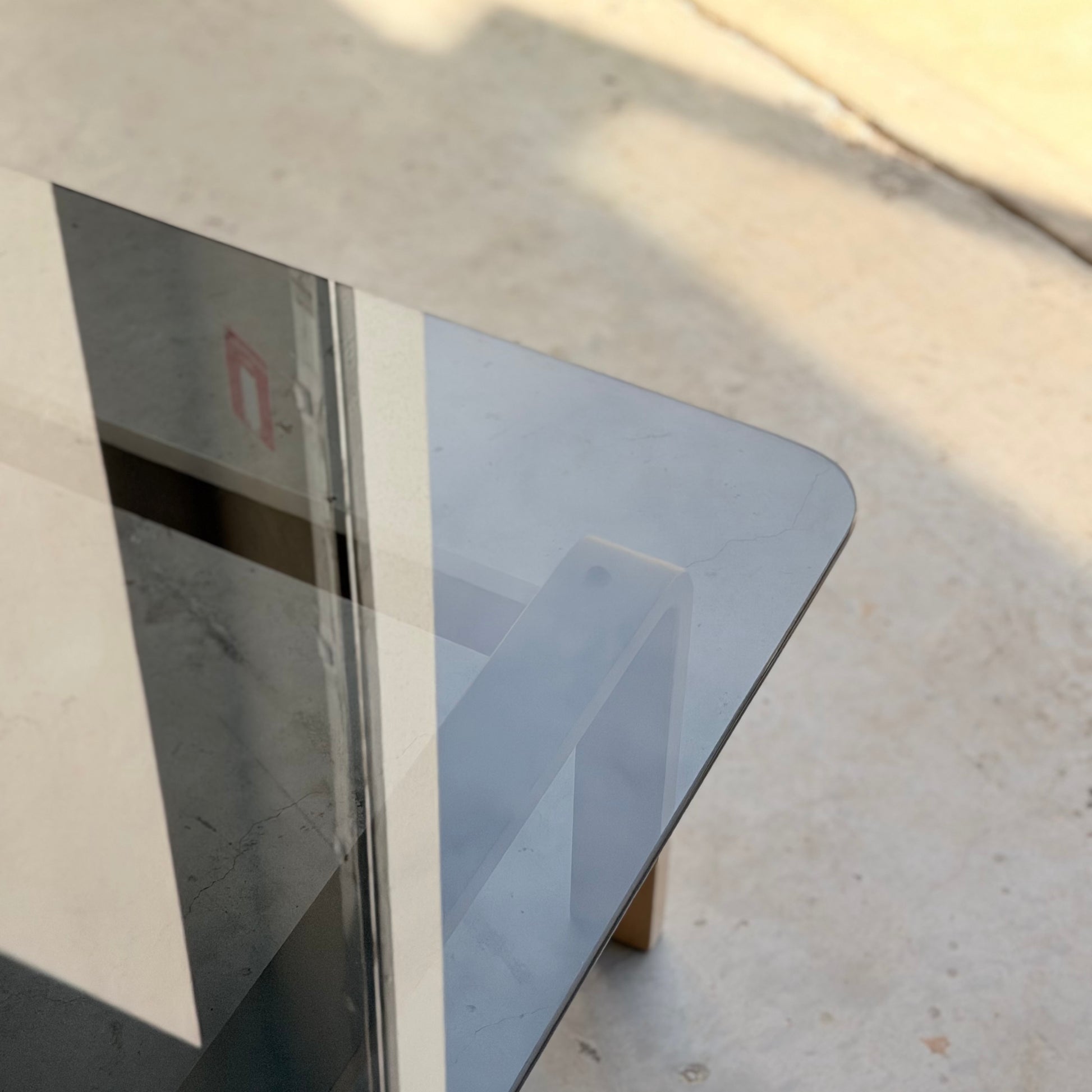 A close-up of a glass-topped table with wooden legs casts shadows on a light floor, sunlight highlighting geometric patterns that evoke the mid-century modern aesthetic of the Tessa Ferrara Lounge Suite – Complete 5-Piece Set (Revive).