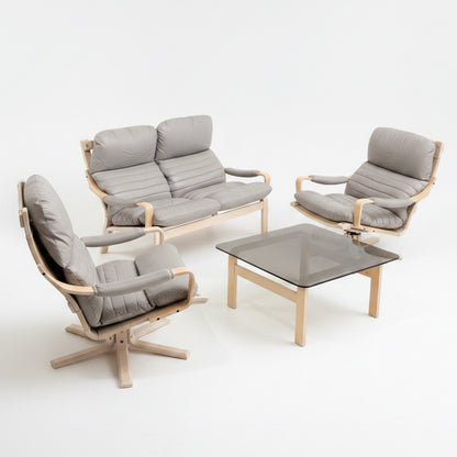 A modern living room set, inspired by mid-century design, features the Tessa Ferrara Lounge Suite – Complete 5-Piece Set (Revive) in light gray and a square glass coffee table with wooden legs on a concrete floor beside a wall and green bin.