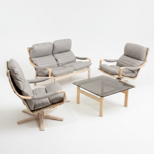 A modern living room set, inspired by mid-century design, features the Tessa Ferrara Lounge Suite – Complete 5-Piece Set (Revive) in light gray and a square glass coffee table with wooden legs on a concrete floor beside a wall and green bin.