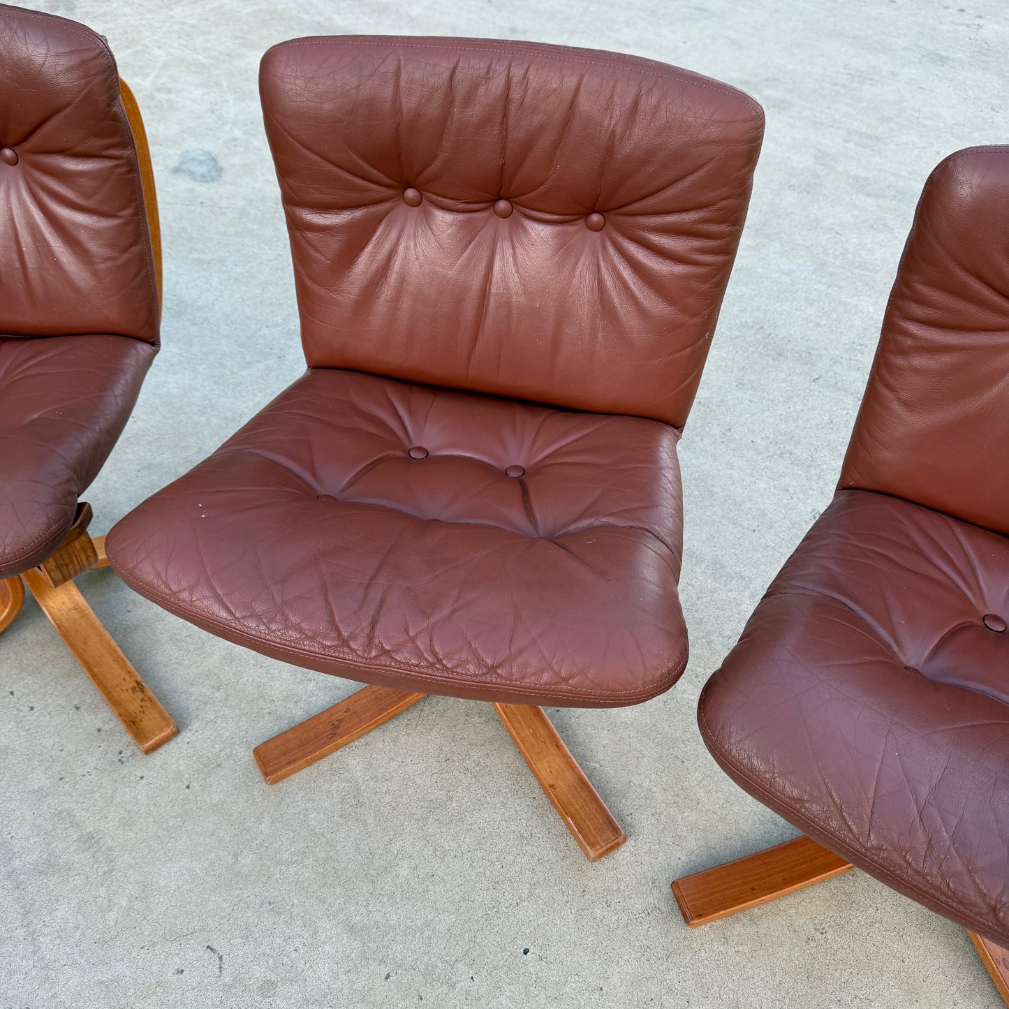 A rare set of 4 vintage Joe Rufenacht lounge chairs in Howe leather, each with tufted backs and seats on four-legged wooden bases, is displayed on a light concrete surface, reflecting a Scandinavian-inspired design.