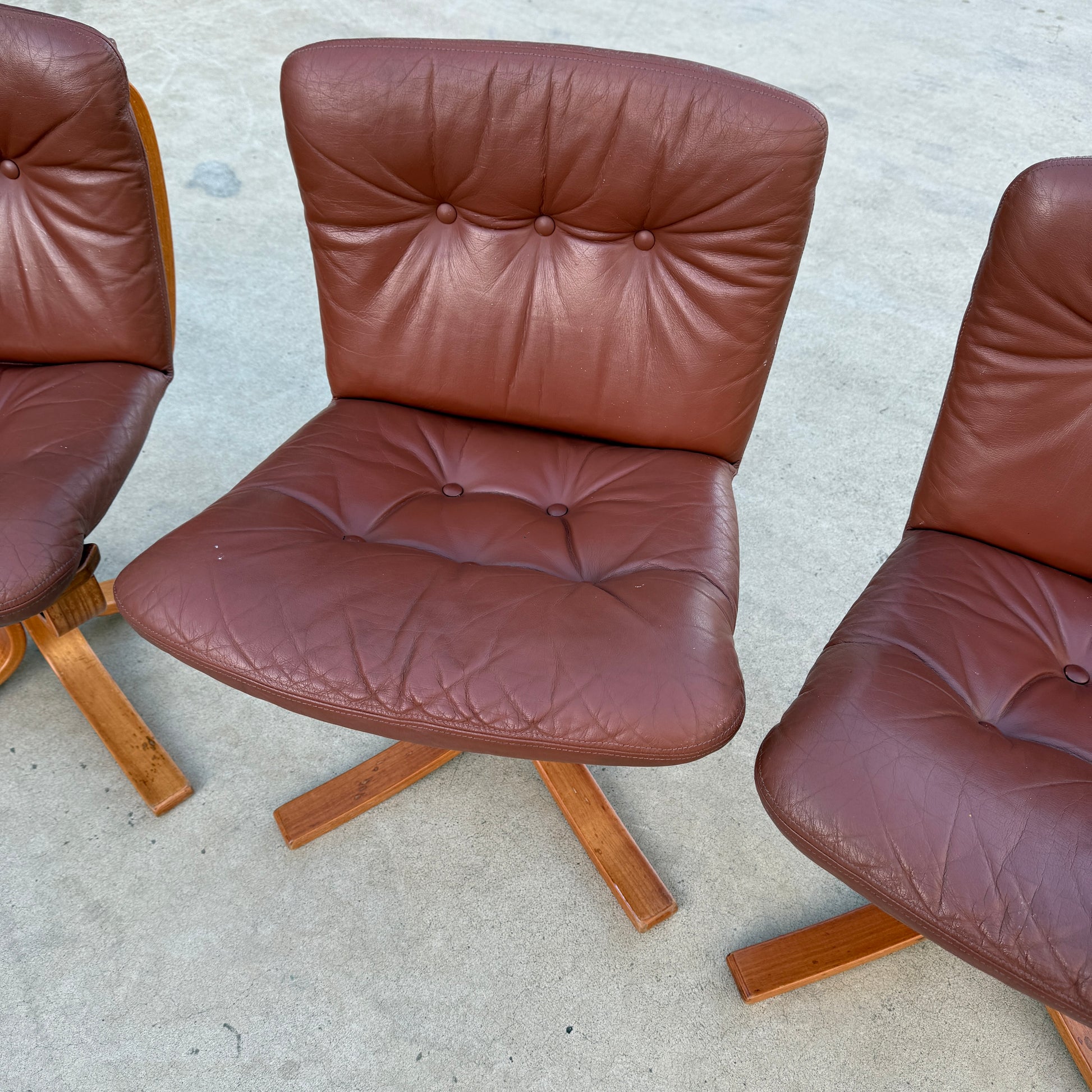 A rare set of 4 vintage Joe Rufenacht lounge chairs in Howe leather, each with tufted backs and seats on four-legged wooden bases, is displayed on a light concrete surface, reflecting a Scandinavian-inspired design.