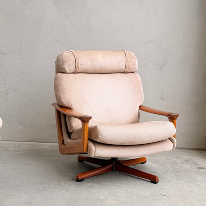 A Vintage Mid Century Tessa T21 Swivel Chair (Revive) with cream velvet upholstery and wooden armrests and base rests on a concrete floor before a plain light gray wall, showcasing timeless mid-century elegance.