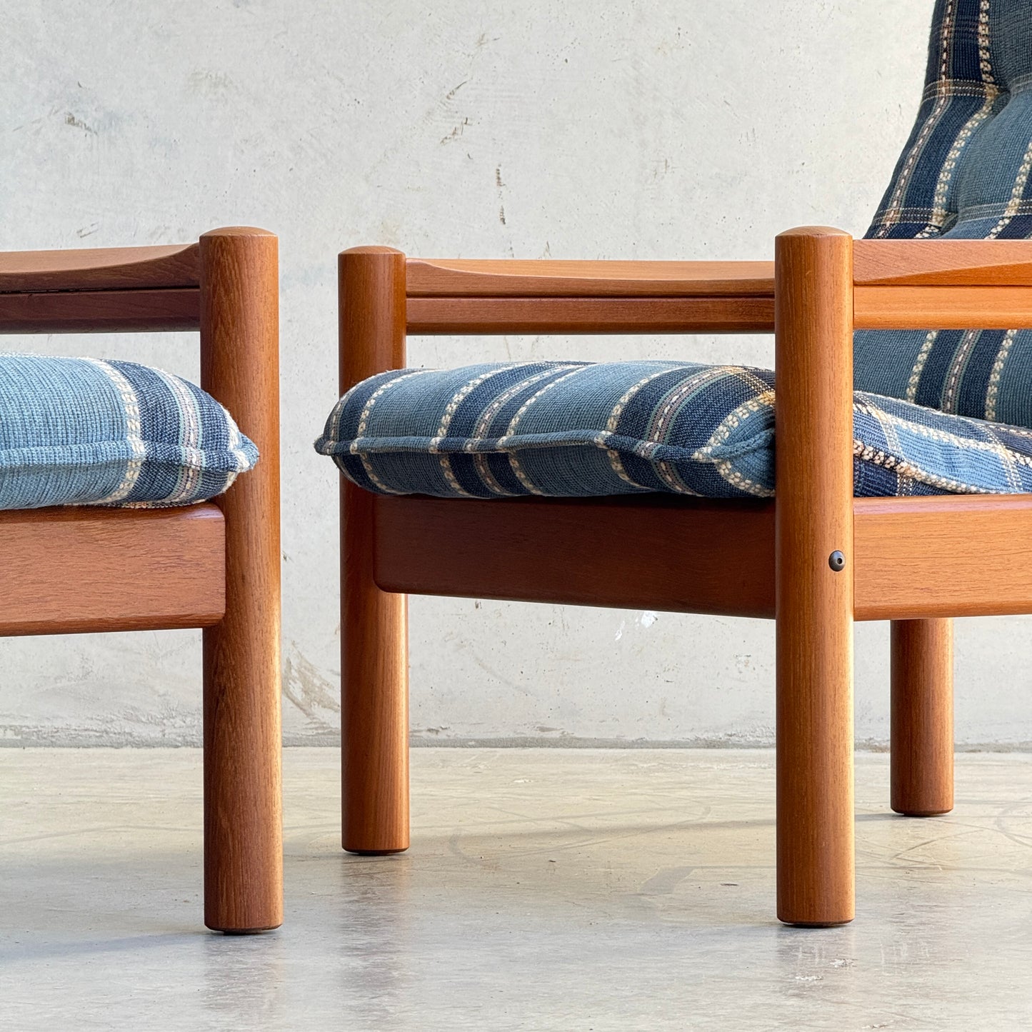 A pair of Restored Domino Møbler Armchairs – Blue Plaid Mid-Century Set (Rediscover) with round legs are placed side by side on a light floor, against a plain, light wall.