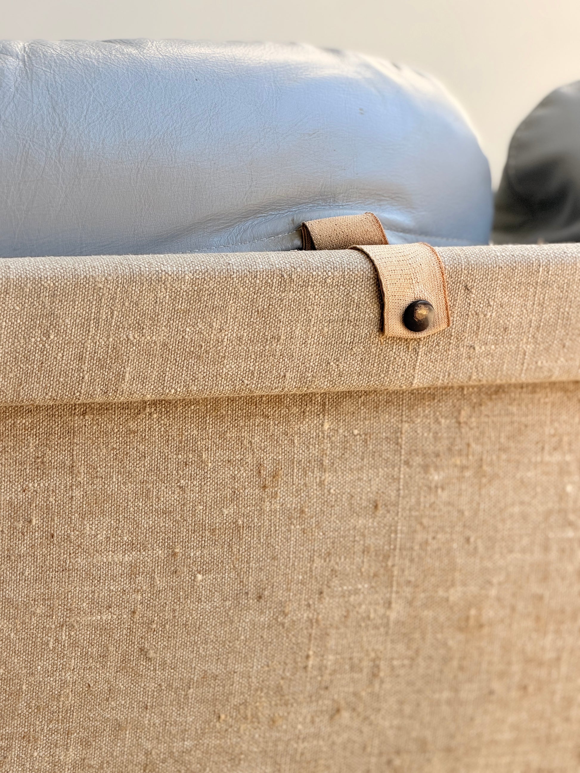 Close-up of the back of a beige fabric chair from the Tessa Ferrara Lounge Suite – Complete 5-Piece Set (Revive), featuring leather strap and metal rivet details with light grey headrest—showcasing Fred Lowen's mid-century modern design.