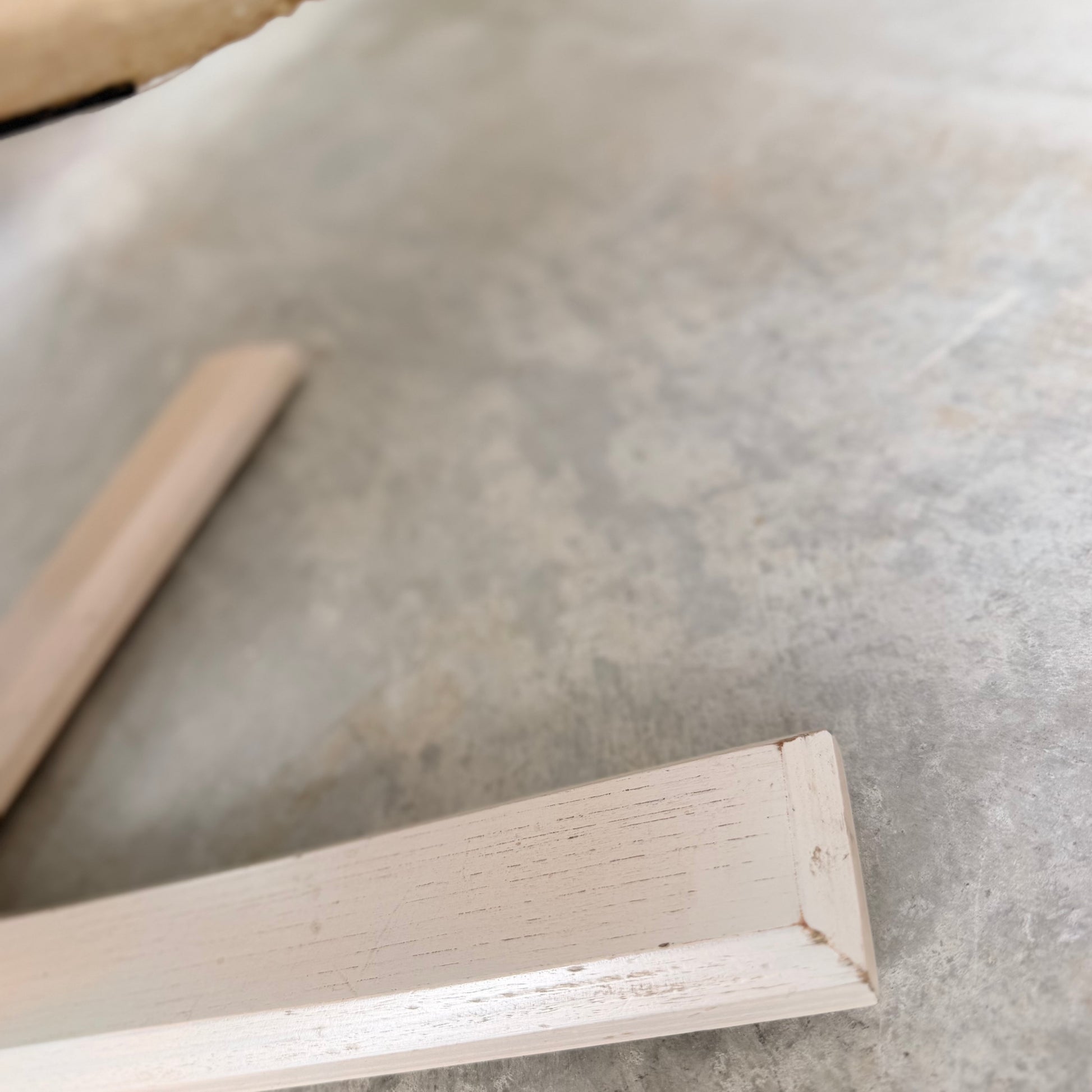 Close-up of two white wooden legs from the Pair of Tessa Ferrara Swivel Armchairs (Revive), set on a textured light gray concrete floor. The slightly blurred image highlights surface details and mid-century Australian design influences.