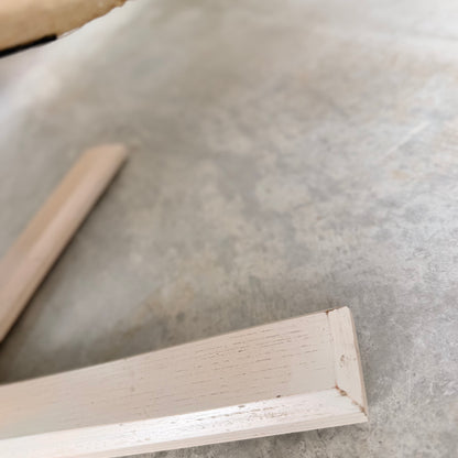 Close-up of two white wooden legs from the Pair of Tessa Ferrara Swivel Armchairs (Revive), set on a textured light gray concrete floor. The slightly blurred image highlights surface details and mid-century Australian design influences.